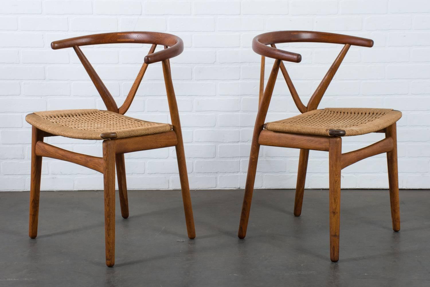 This pair of Mid-Century Modern chairs were designed by Henning Kjærnulf for Bruno Hansen, Denmark, circa 1960's. They feature solid teak frames with curved backrests and beautiful joinery. The original paper cord seats have vintage wear such as