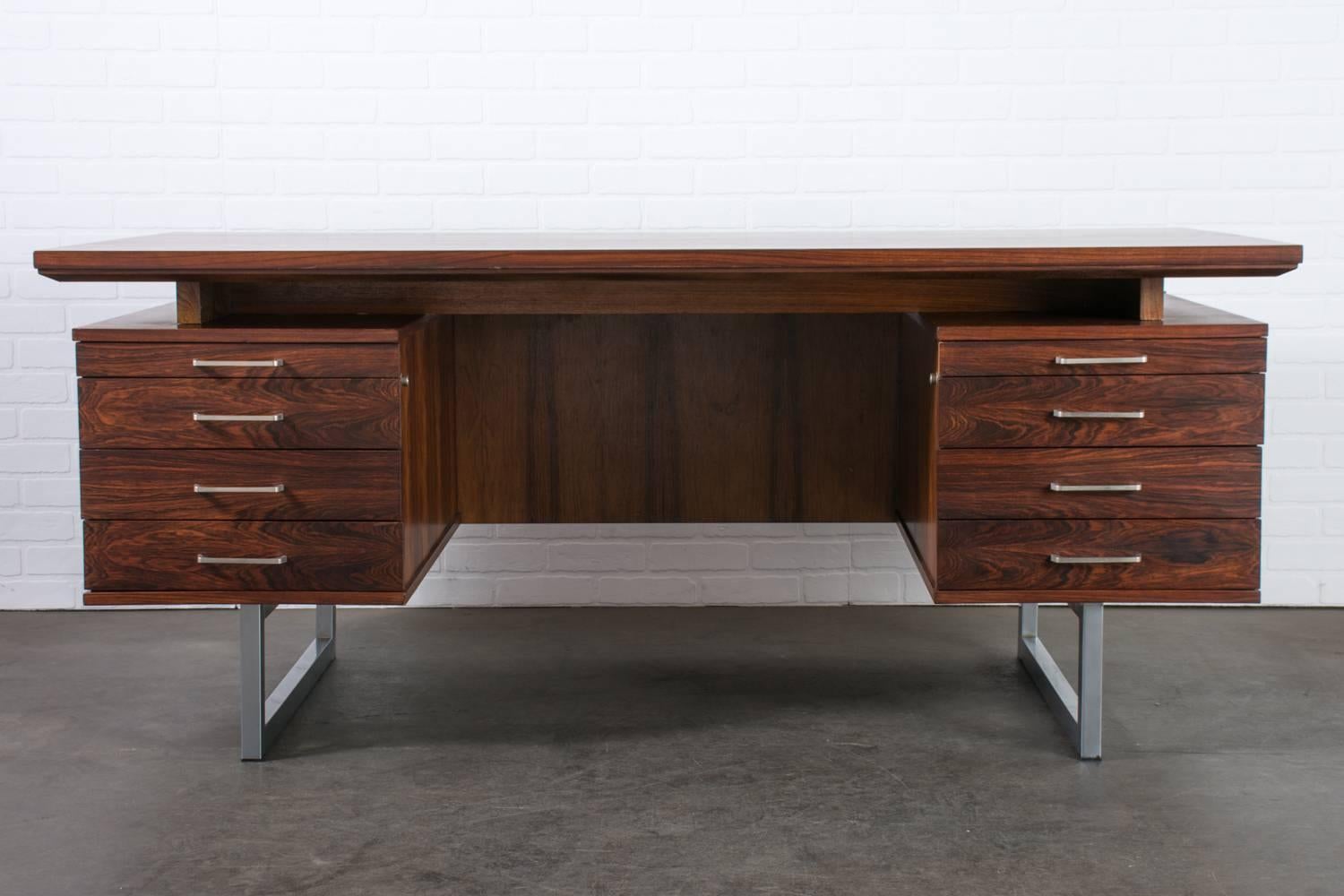 This vintage Mid-Century rosewood executive desk features a floating top, six drawers, two pull out trays, and steel legs and drawer pulls. The bottom three drawers on each side have adjustable dividers (a total of ten dividers included that fit in