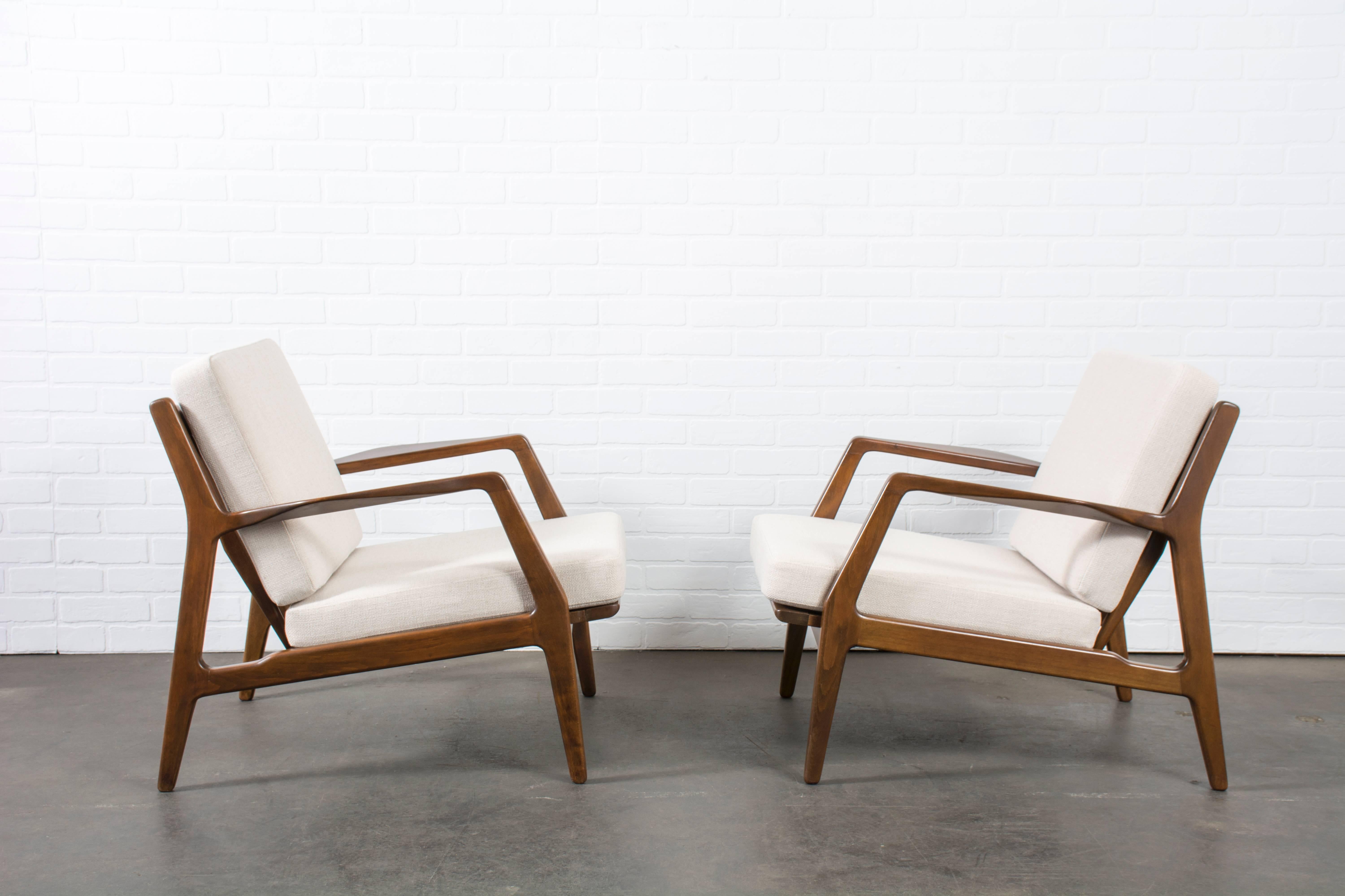 This is a pair of vintage Mid-Century lounge chairs by Ib Kofod Larsen. The frames have a walnut finish. Original straps. New cushions and upholstery.