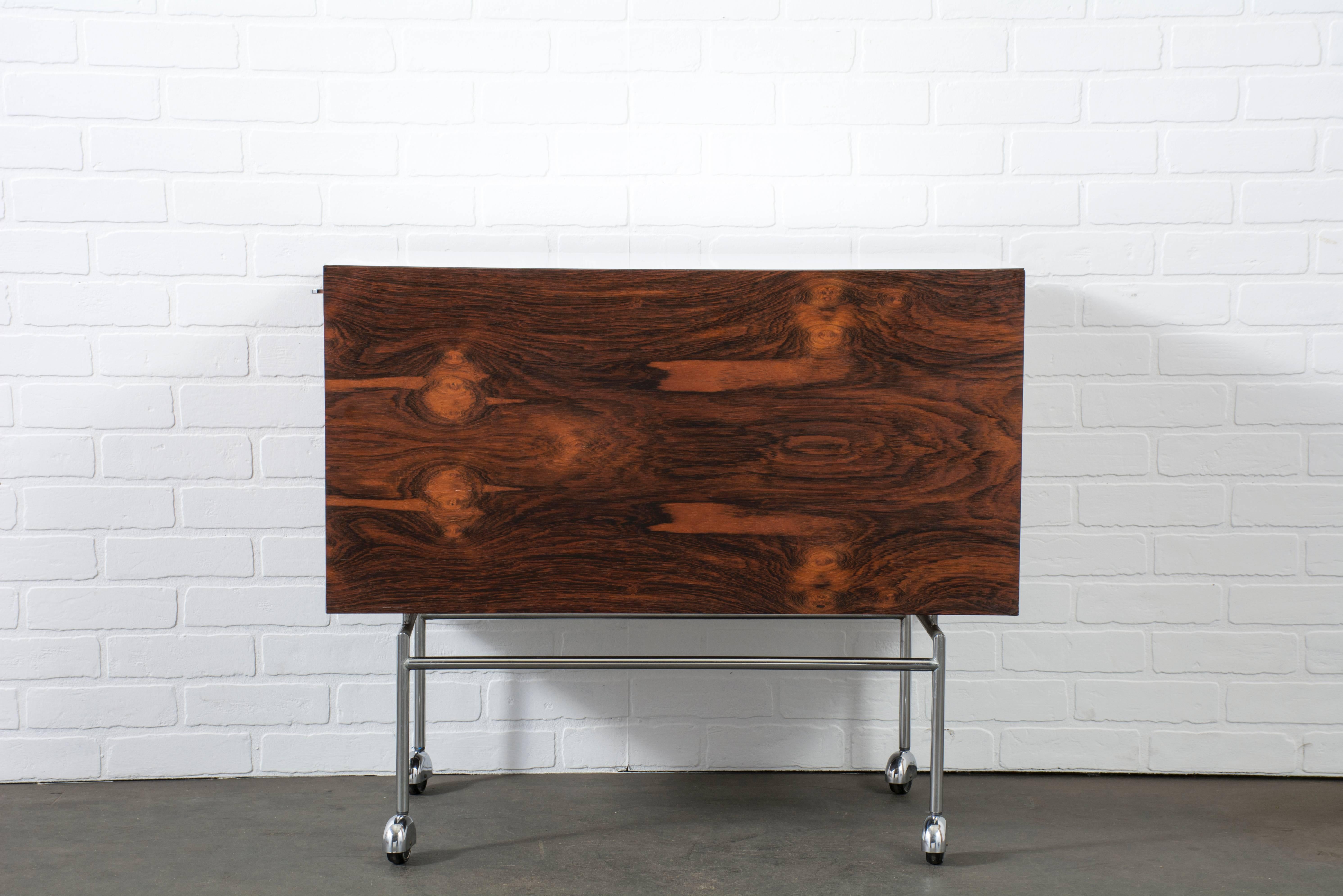 This vintage Mid-Century liquor cabinet was designed by Poul Nørreklit in the 1960s. It is Brazilian rosewood with a white laminate top that slides out to one side to reveal a large storage compartment (can hold 30+ bottles) and a removable rosewood