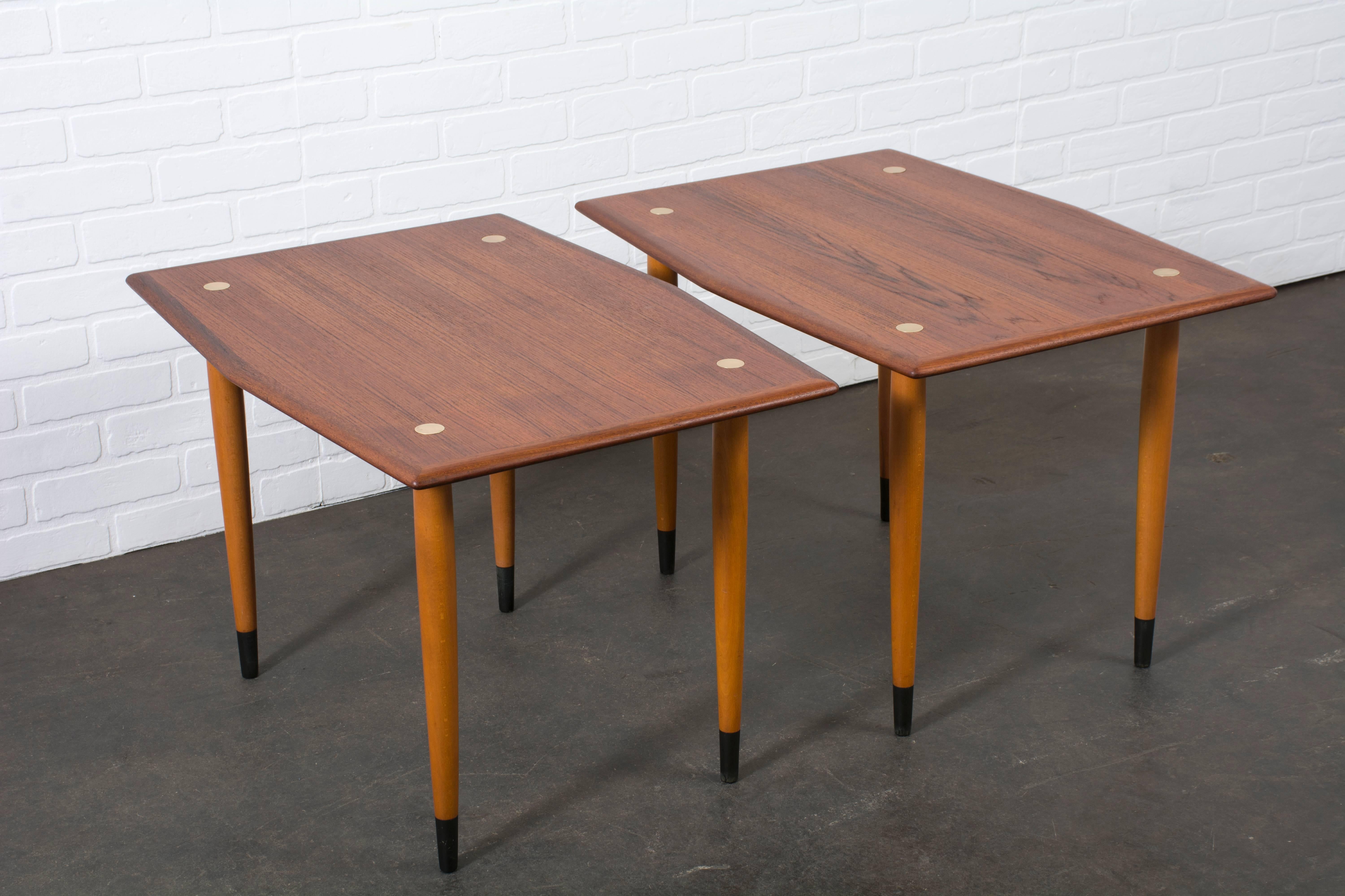 This is a pair of Mid-Century Modern teak and beech end tables by DUX, made in Sweden, circa 1950s. They have circular brass inserts on the teak tops and black ebonized tips on the beech legs.