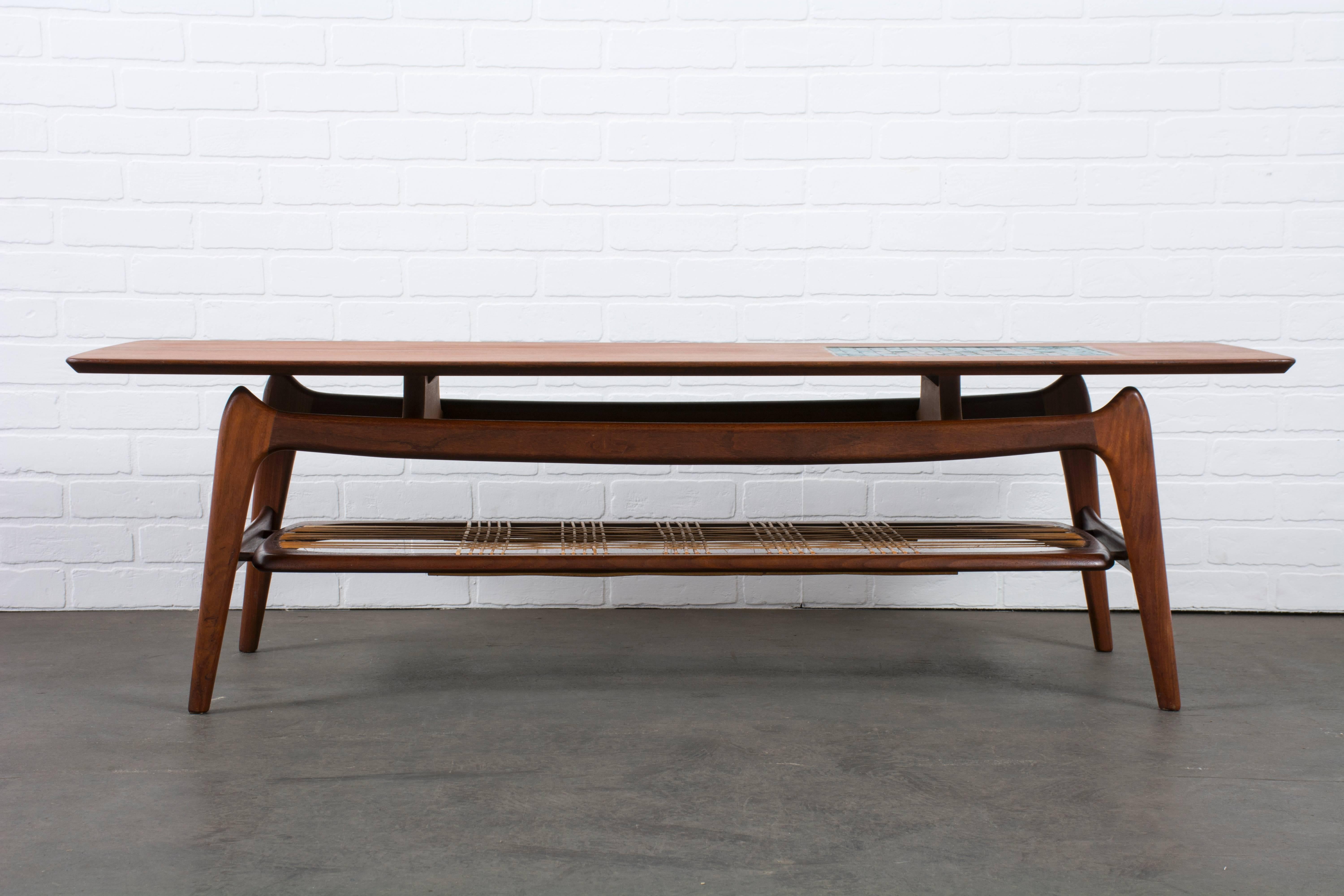 This sculptural teak coffee table was designed by Louis Van Teeffelen for Wébé Meubelen (Netherlands) in the 1950s. It has a glass tile inlay on the top and a Minimalist rattan shelf below. Labeled Wébé Meubelen.
