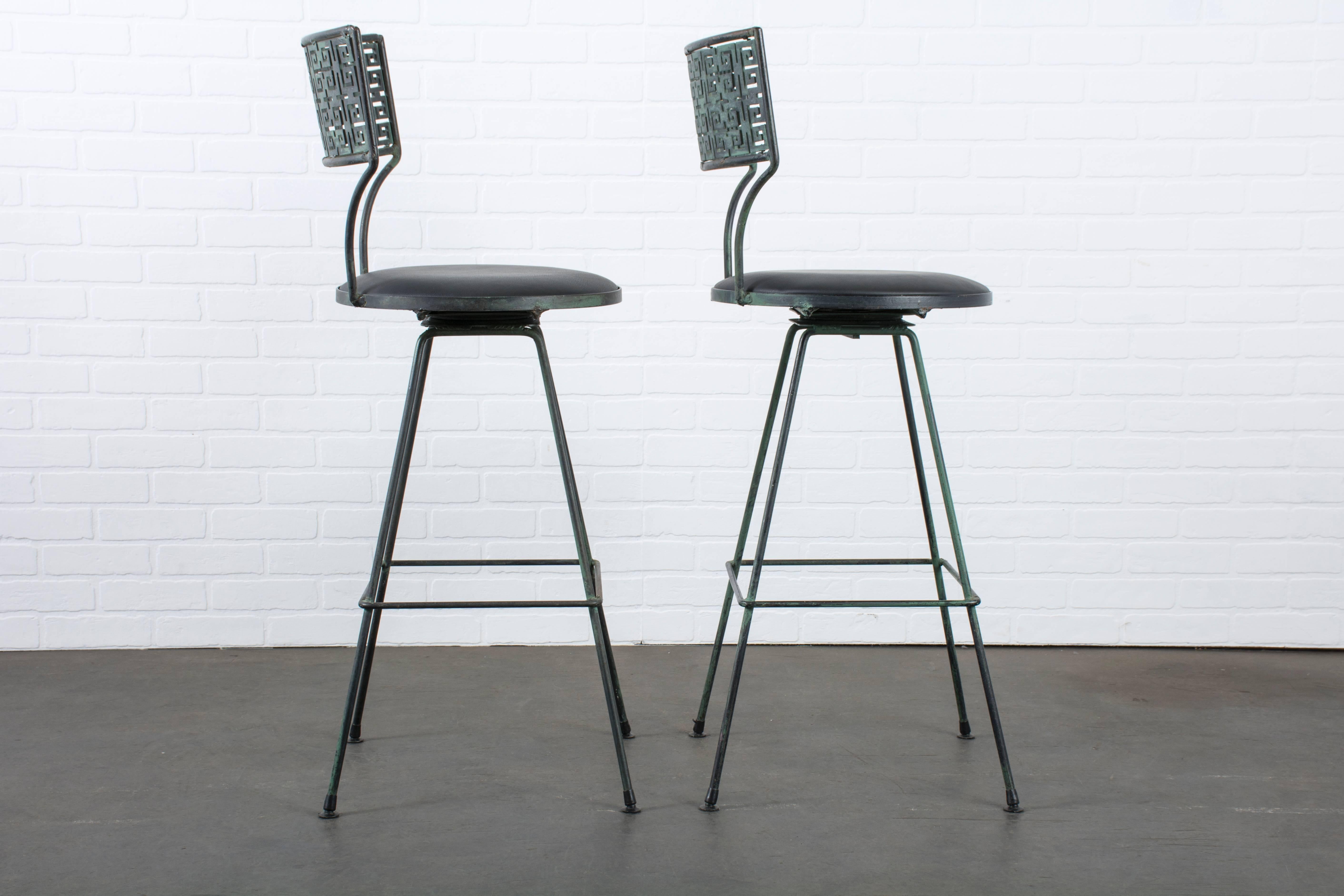 This is a pair of vintage Mid-Century swivel bar stools. The frames are black wrought iron with a green patina and the seats have been professionally reupholstered in black leather.