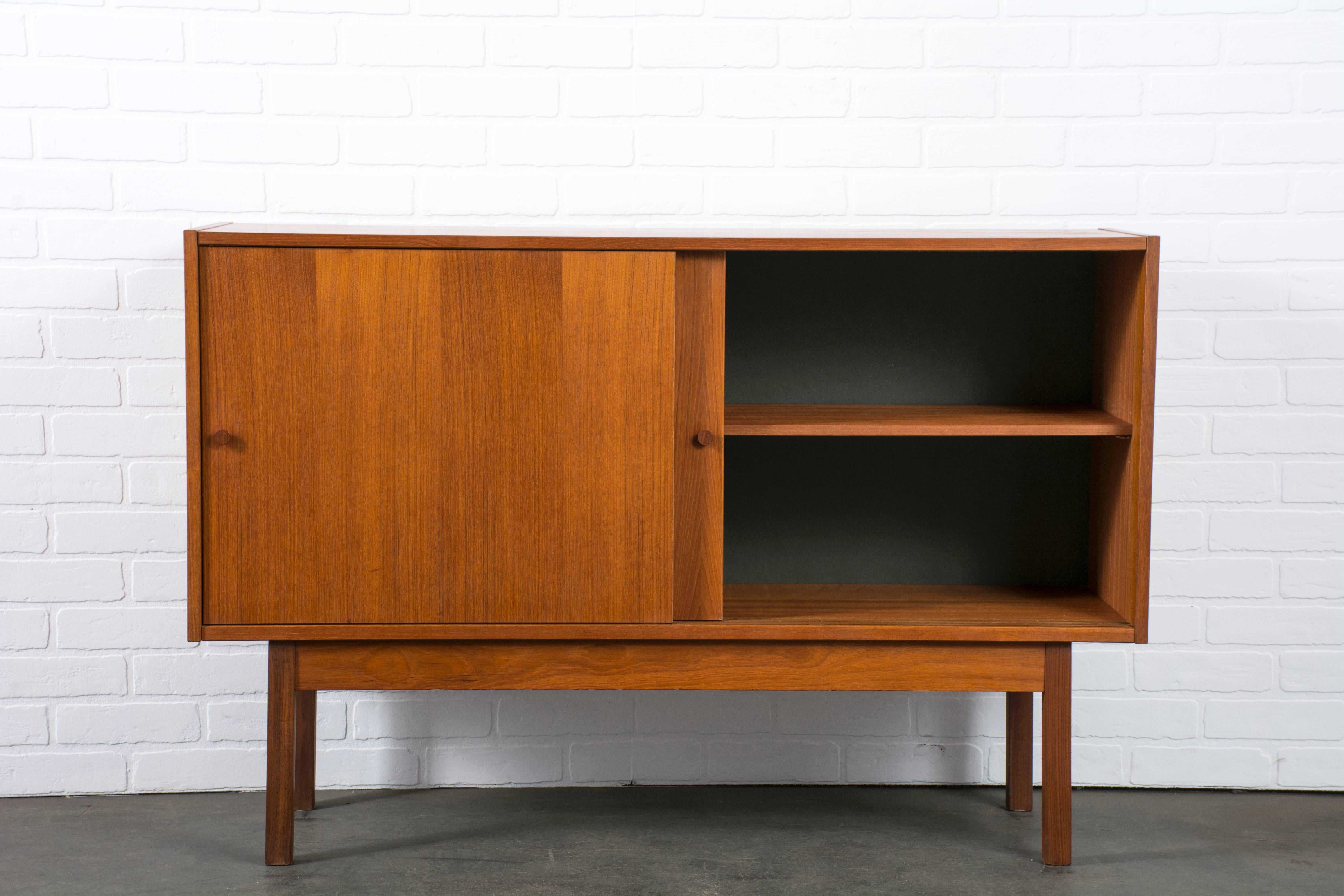 This vintage Mid-Century teak sideboard features two sliding doors and one shelf.
