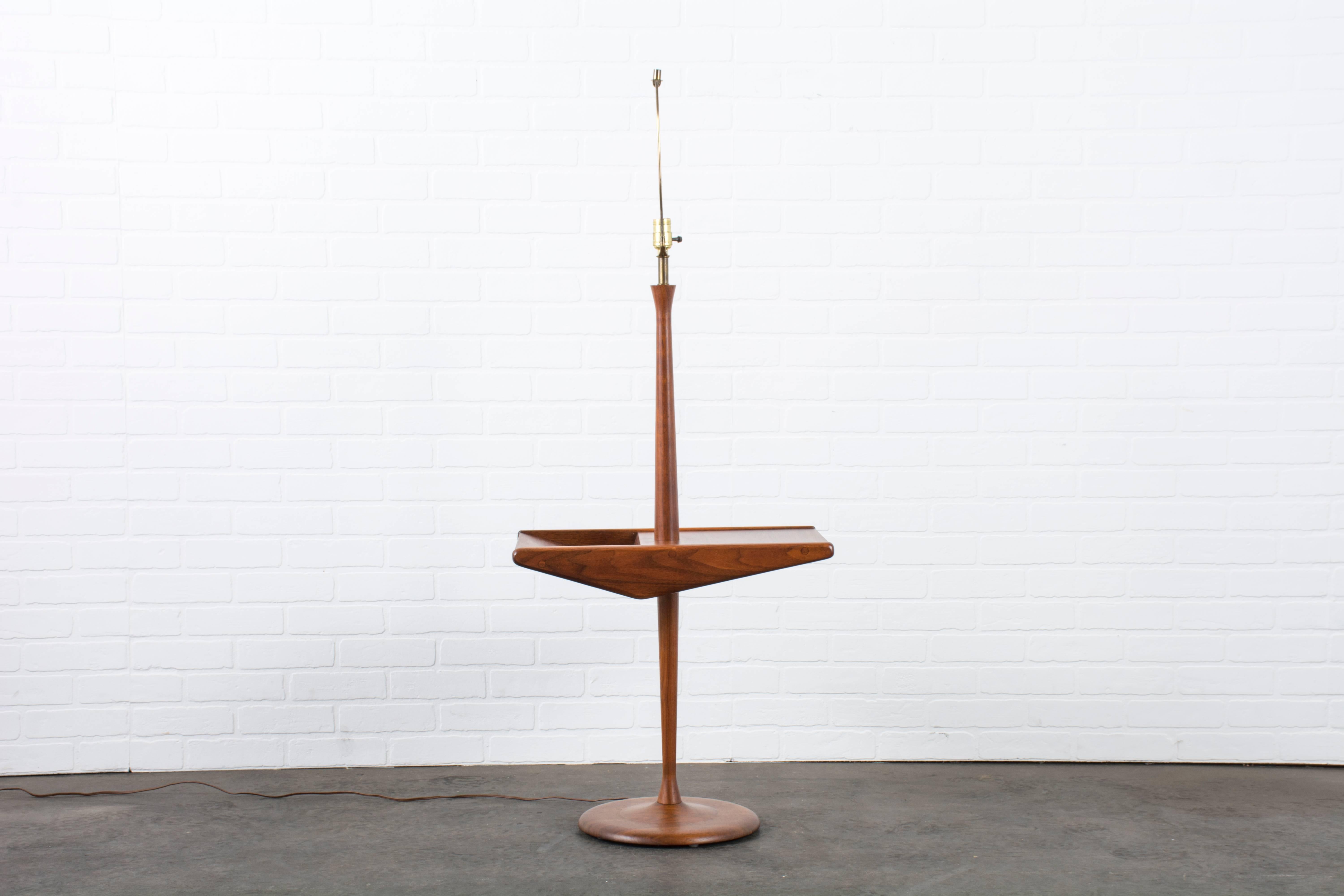 This Mid-Century Modern walnut floor lamp by Laurel Lamp Company features a sculptural side table with a space to hold books or magazines. Shade not included, circa 1960s. Measurements: approximately 53.5