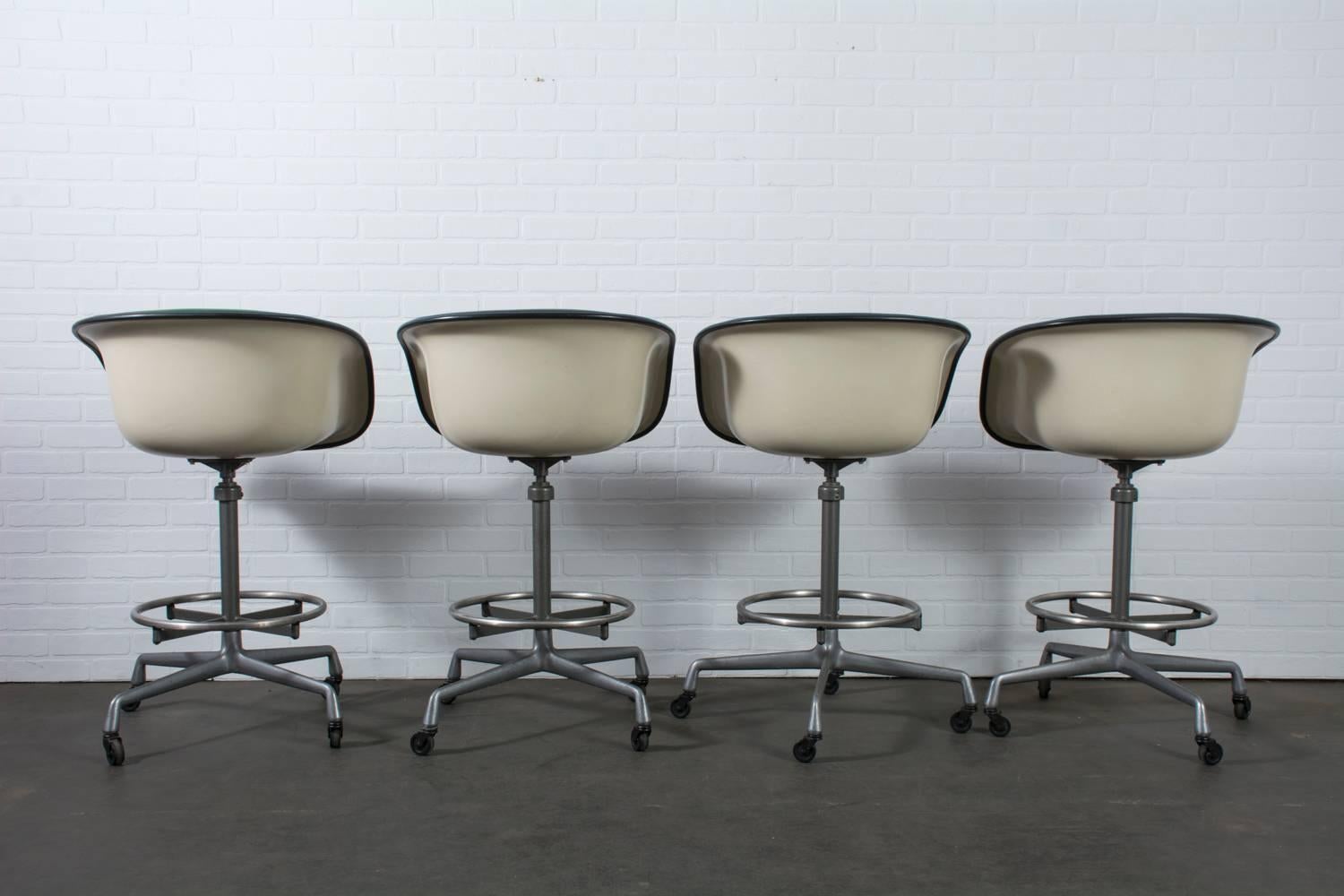 This set of four Mid-Century Modern stools was designed by Charles and Ray Eames. They feature Herman Miller cast aluminum and enameled steel secretarial stool bases that rest on four rubber casters (model EC123-36) and La Fonda armchair seats with
