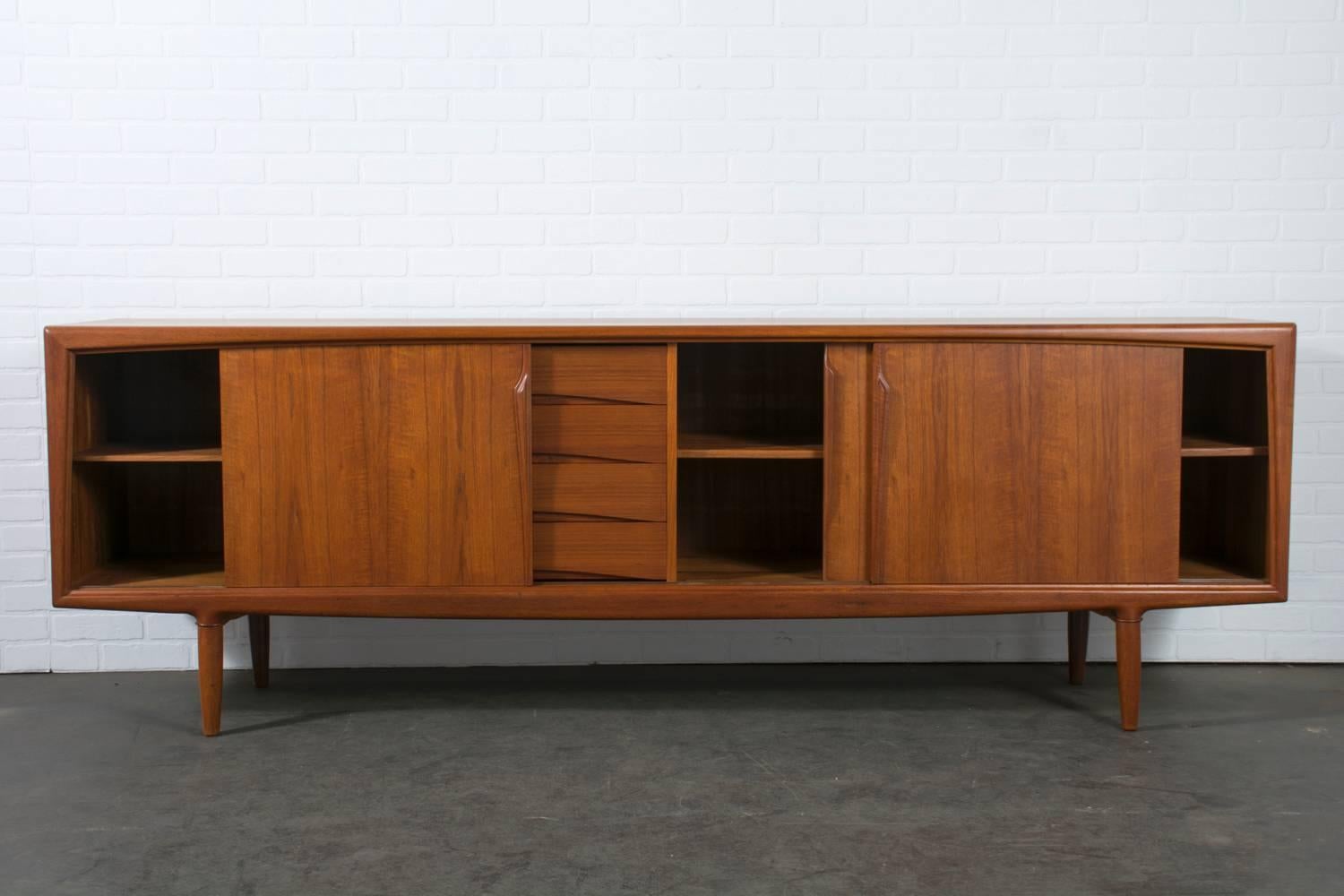This vintage Mid-Century teak credenza was designed by Gunni Omann and manufactured by Axel Christiansen Odder in the 1960s. It features three sliding doors with sculptural handles that conceal two shelves, and four drawers. Beautiful details