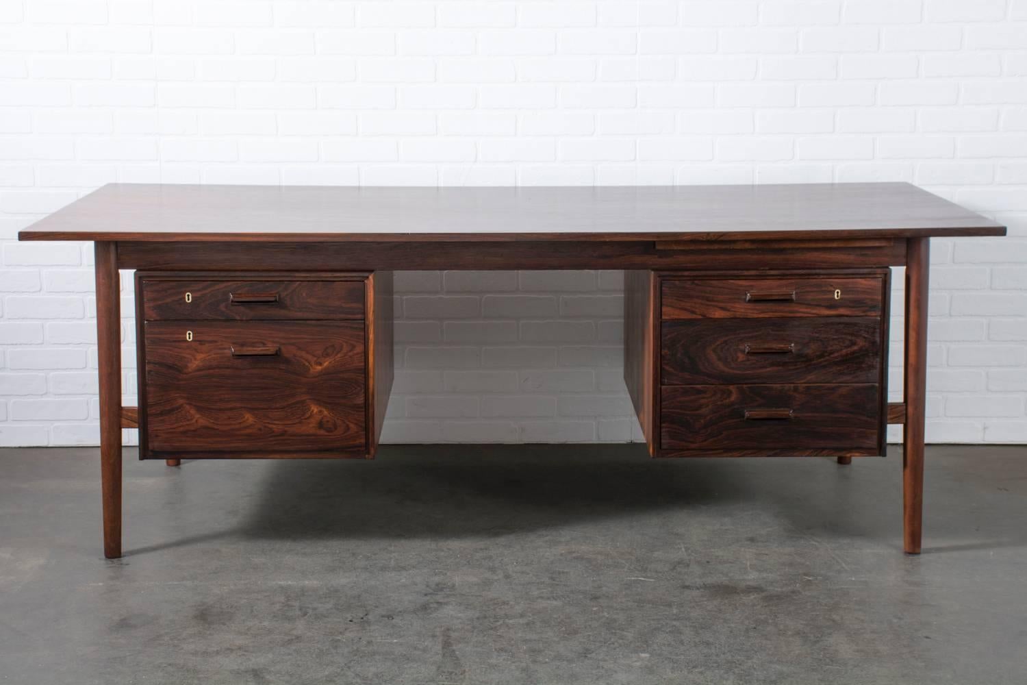 This Danish Modern rosewood desk features three drawers on the right side (the top one with a removable rosewood tray) and two drawers on the left side, the bottom of which is a file drawer. This 'partner' desk can be used from both sides. The back