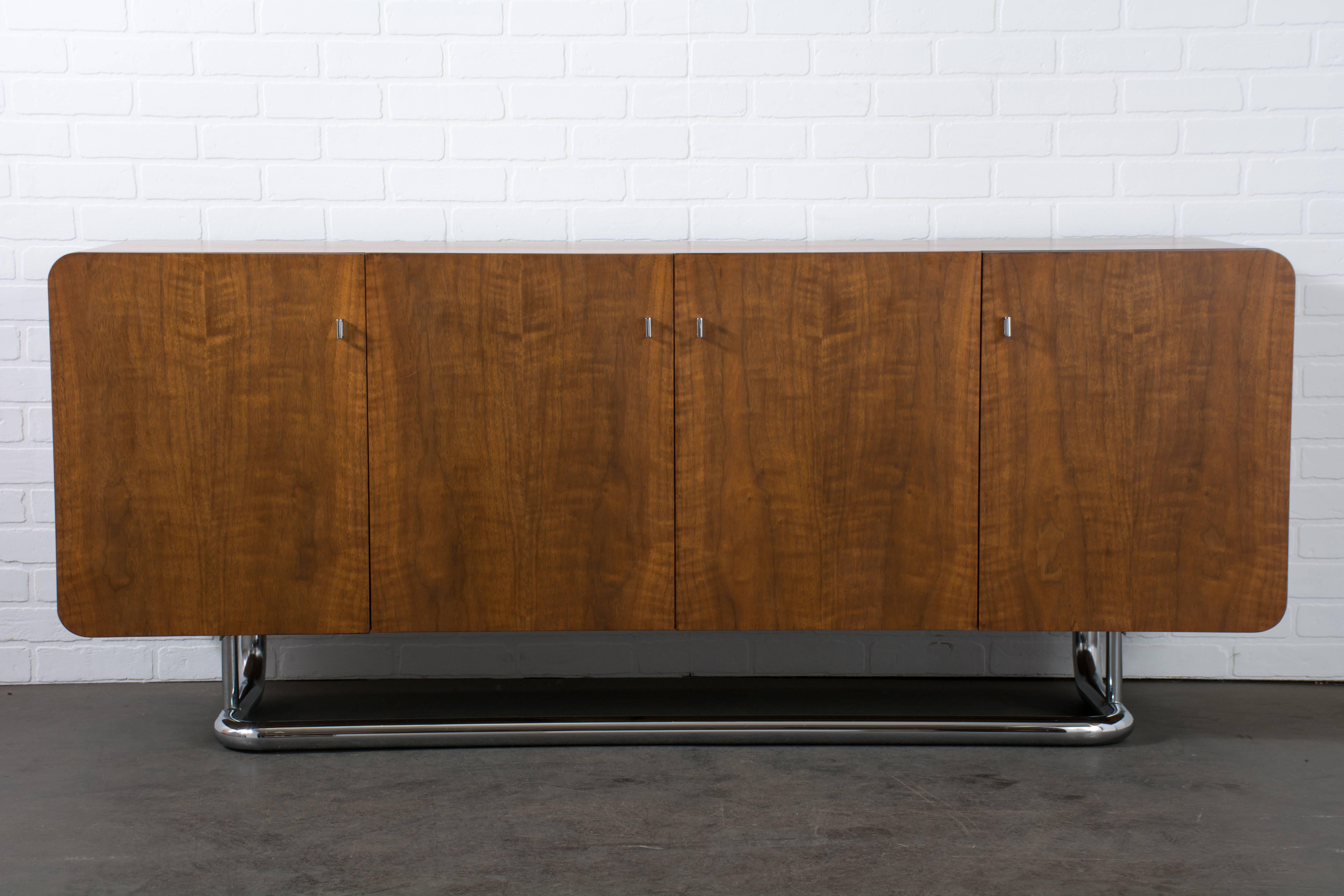 This Mid-Century Modern walnut sideboard was designed by Jack Cartwright for Founders, USA, circa 1970s. It features four doors that conceal three drawers in the middle and an adjustable shelf on each side. This piece has unique details such as