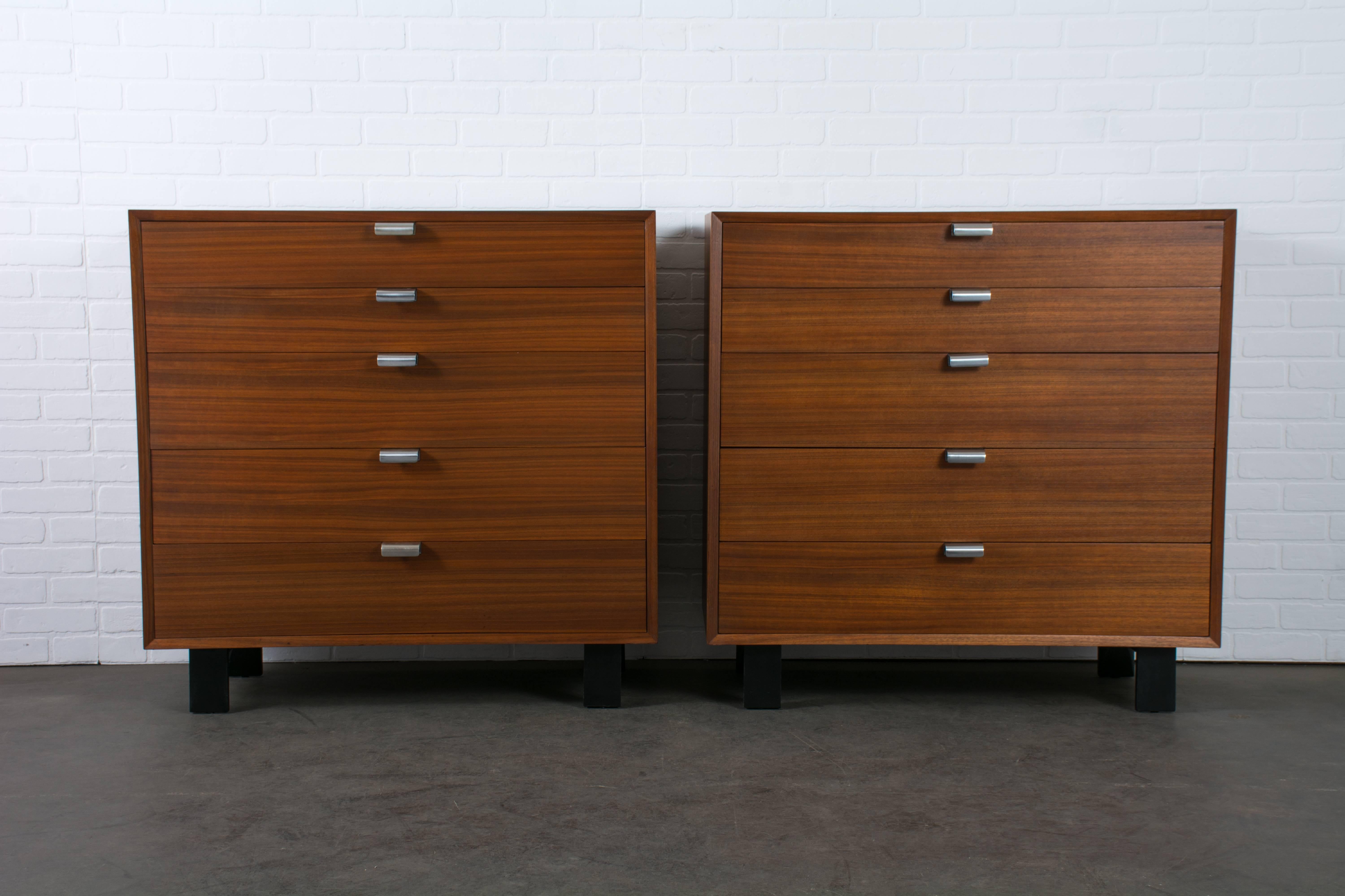 These Mid-Century Modern dressers were designed by George Nelson for Herman Miller in the 1950's. They are walnut with black legs and metal handles with a chrome finish. There are dividers in the top and middle drawers. This pair of matching
