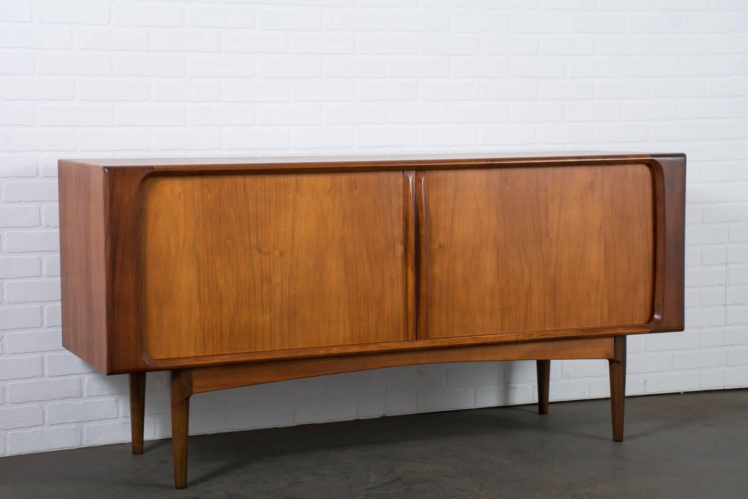 This Danish Modern teak credenza is by Bernard Pedersen & Son, circa 1960s. This sideboard features tambour doors that slide smoothly to reveal three slim tray drawers and three adjustable shelves.