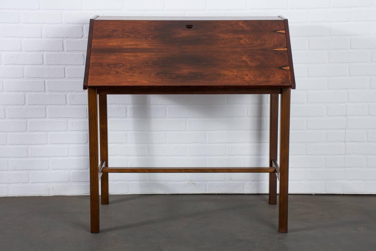 This Scandinavian modern rosewood desk has a folding top, perfect for concealing the contents or for compact spaces. Inside the desk there are two drawers and shelves. This vintage Mid-Century desk is finished on the back with beautiful grain