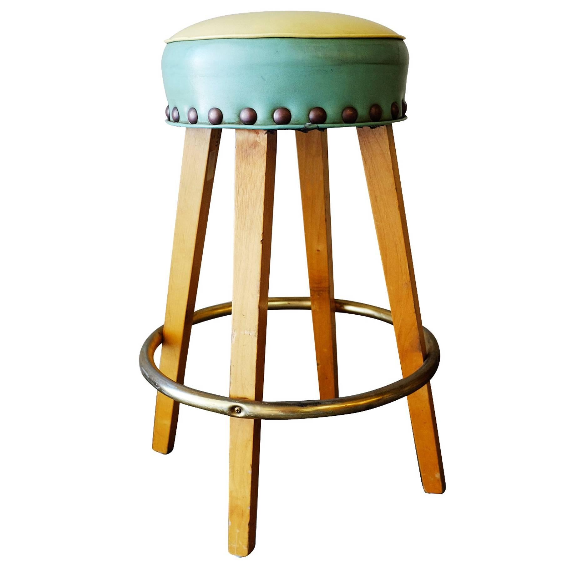 Set of four custom handmade Mid Century style bar stool with tapered oak legs, a round brass footrest that connect to a blue and beige vinyl seat. The seat has wraparound oversized nail head accents.

 