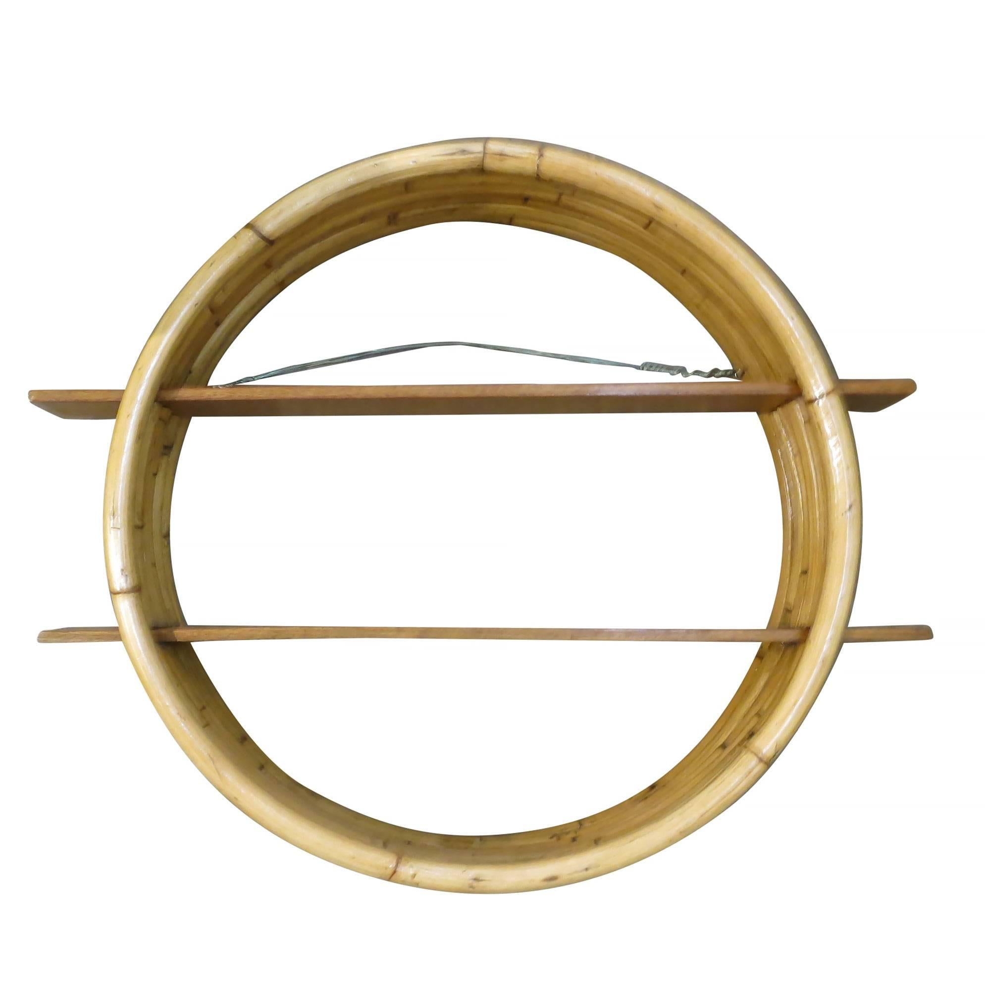 Circular rattan wall self, circa 1950. This rare rattan wall shelf features unique 5 strand stack rattan frame made with cut-out sections which hold two mahogany shelves.

All rattan, bamboo and wicker has been painstakingly refurbished using the