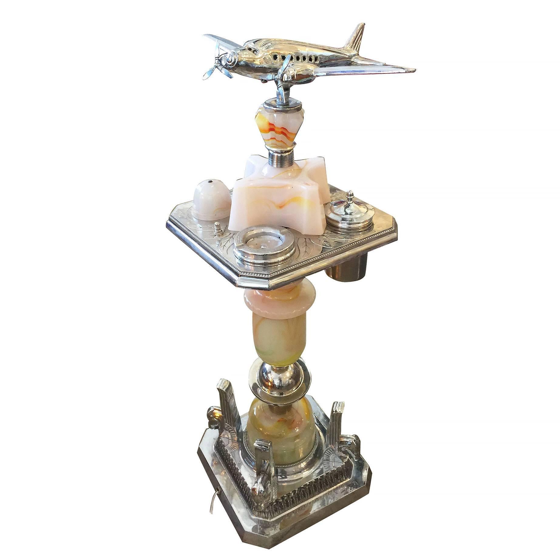 Brass Art Deco ashtray stand featuring a decorative light up airplane on top with a glass light up bass on the bottom. 

The stand comes with a built-in light, two ashtrays and tobacco canister.