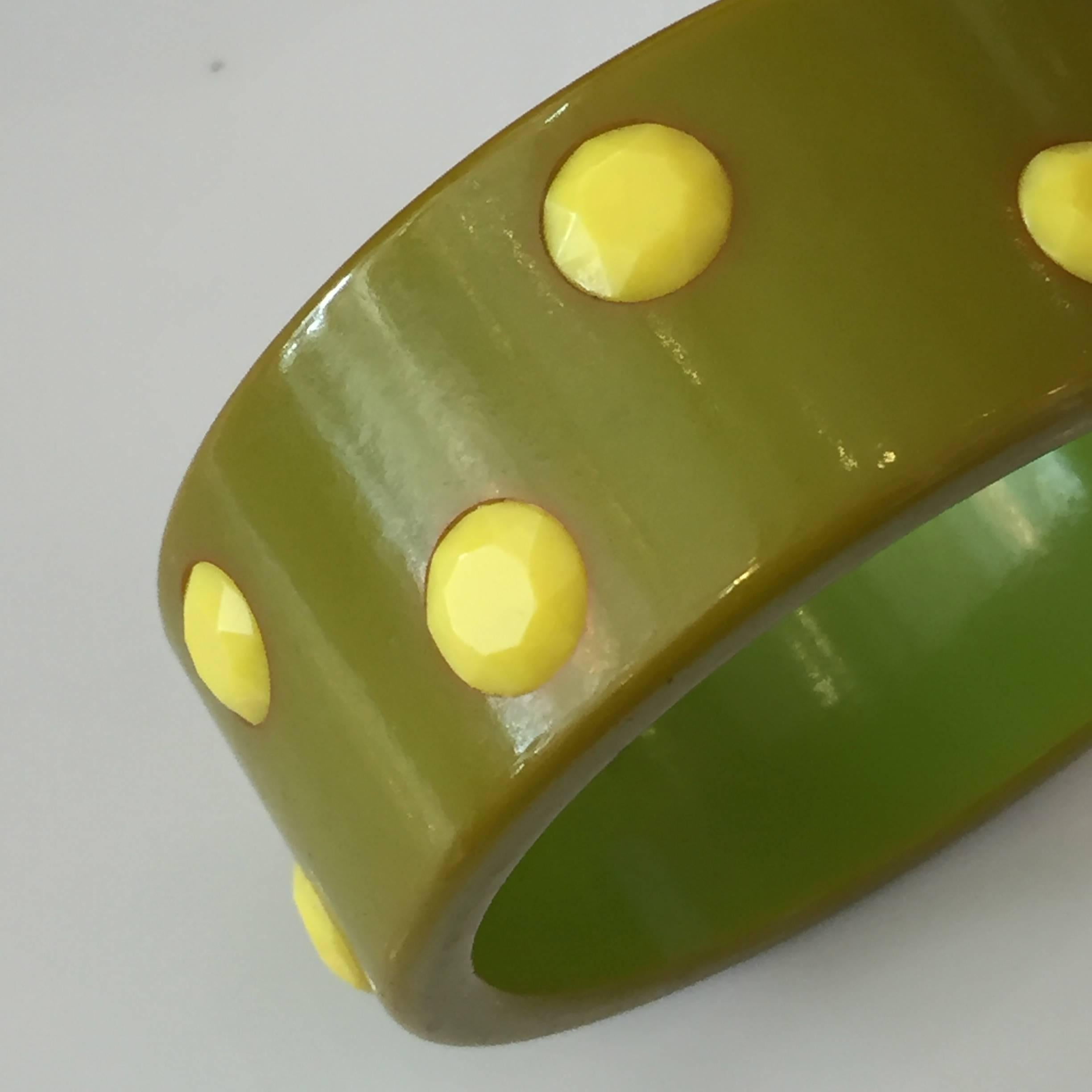 Large green and yellow polka dot bakelite bangle with a darker green on the inside of the bracelet.

The yellow polka dots made of a facetted bakelite rhinestone which adds a nice sparkle to this huge bracelet.

1 1/4