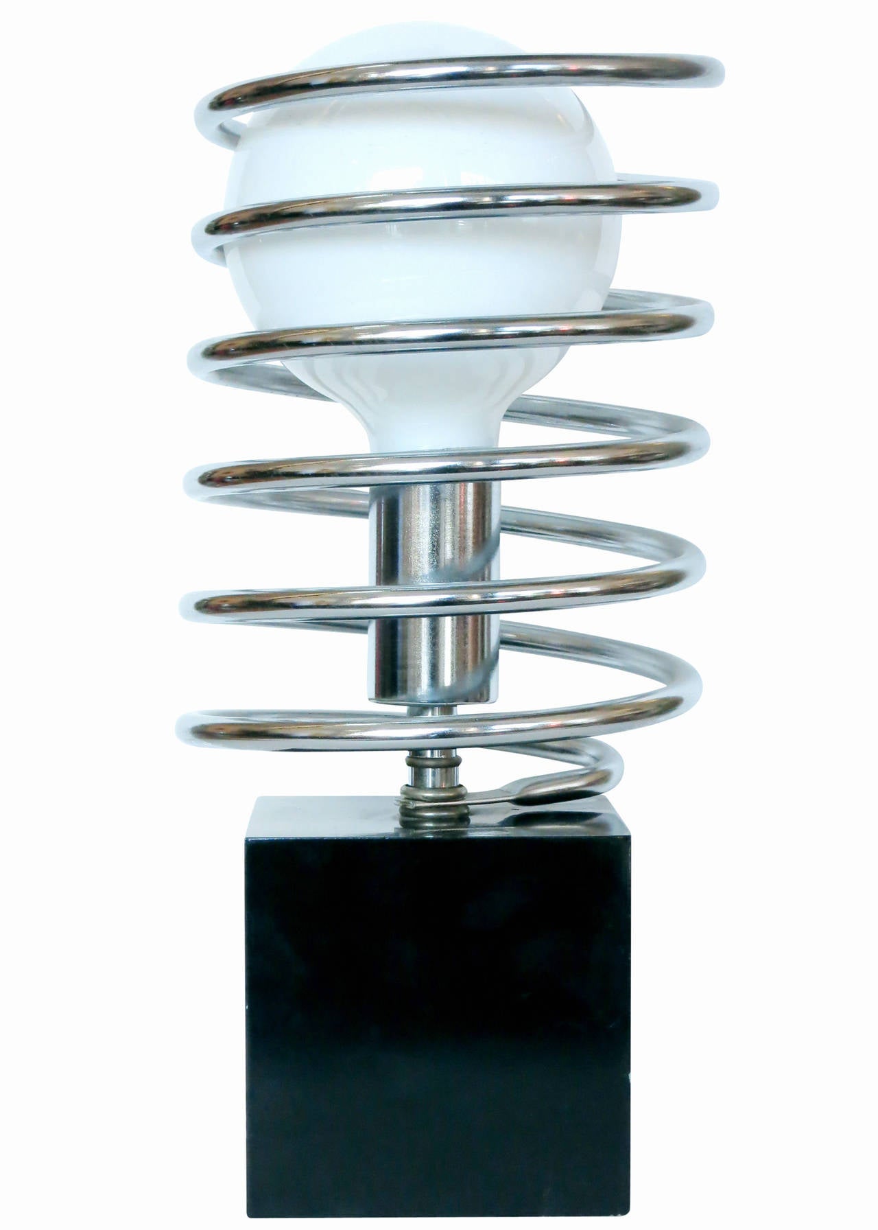 This modernist spring table lamp features a black steel cube with a chrome socket surrounded by a large chrome coil spring. 

It's unique and elegant simplicity is an exquisite example of a late 1960s design by the Sonneman lighting company.