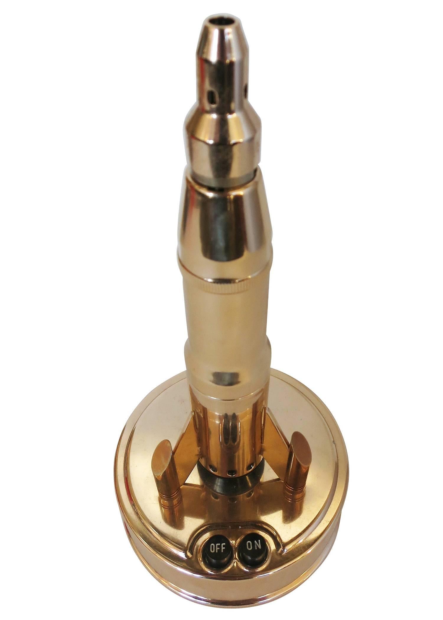 Mid Century brass rocket ship electric butane table lighter by Bronica featuring a large 9' tall brass sculpture of which lights from the top of the lighter. 

Comes new in original display box with instruction manual.

Takes 2 C-cell batteries