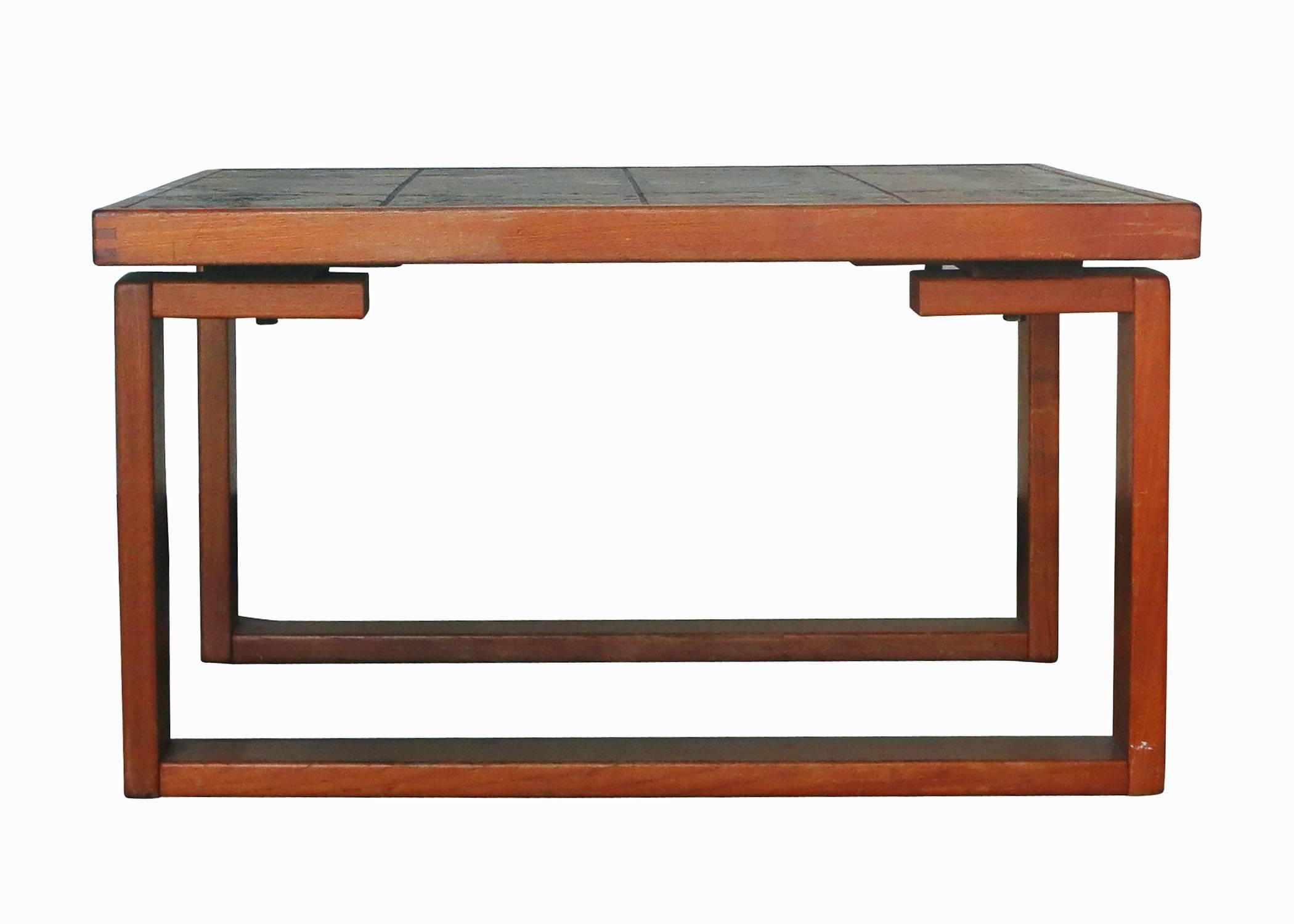 Solid teak table with U shaped legs and textured clay art tile top. The Tile mosaic top is made of cream, red,  brown and green come together in a abstract pattern and sits on a set of off set legs which give the table an almost  floating