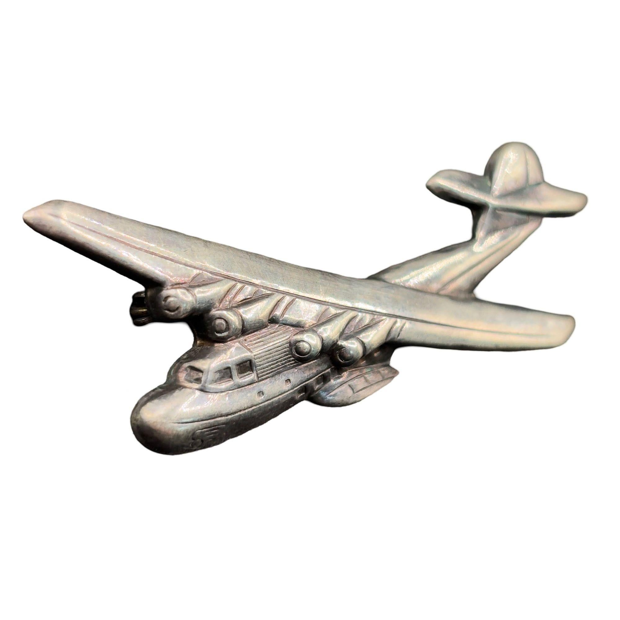 Questa spilla della seconda guerra mondiale rappresenta un pezzo unico della storia della Marina e dell'aviazione degli Stati Uniti. Realizzata in argento sterling, la spilla ha la forma del Martin M-130 Flying Boat, un aereo civile originariamente