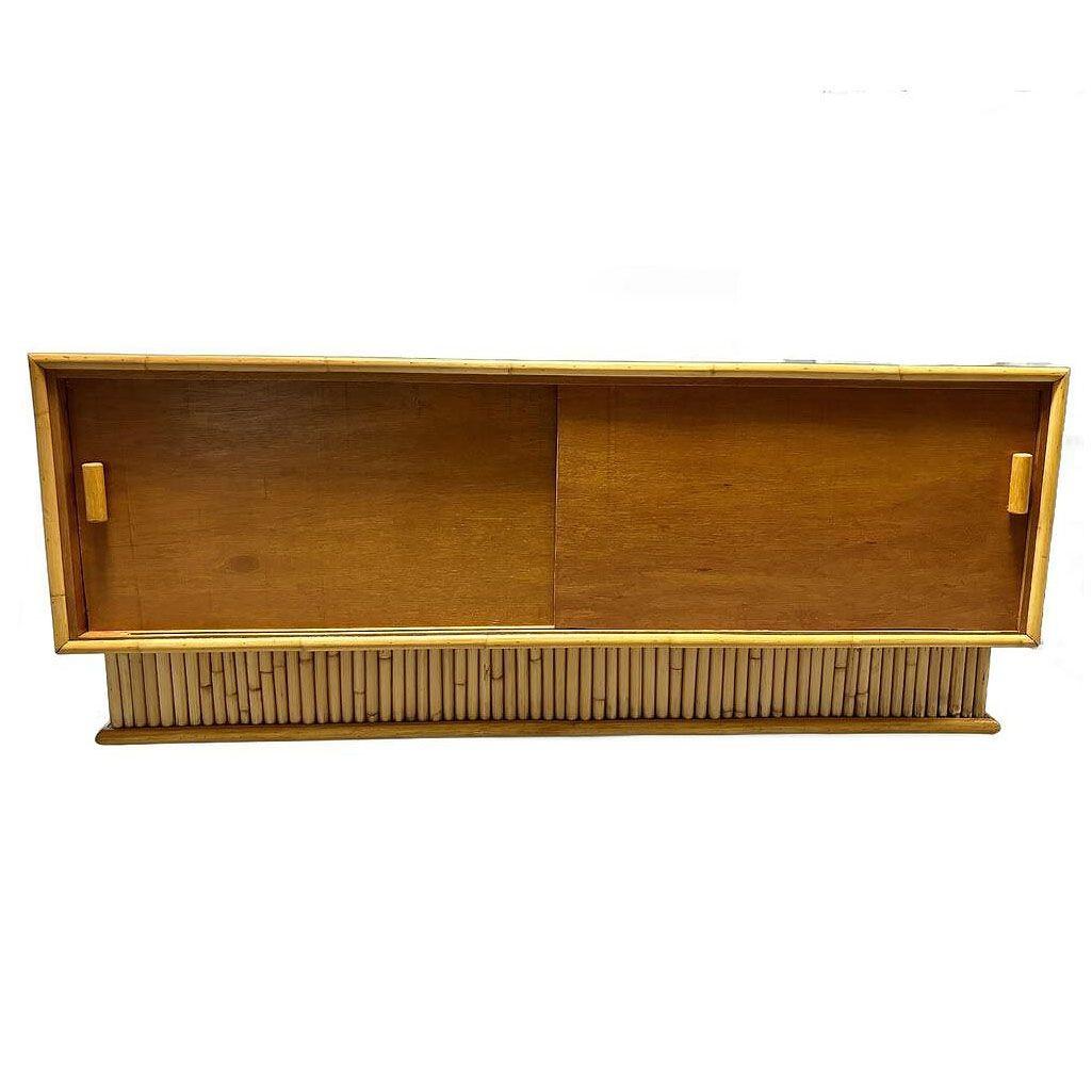 Restored Mid-century mahogany credenza with a stacked rattan base designed after the furniture made famous by Paul Frankl. The credenza features a center bookshelf with two shelves behind 2 sliding doors on each side. It features a Mahogany Top with