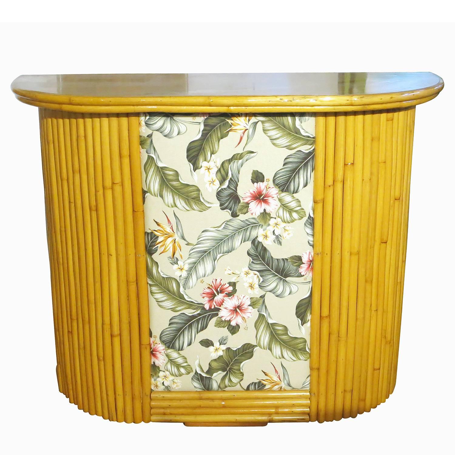 Pole rattan bar with formica top and bark cloth hibiscus print front, circa 1950. The bar features two shelves along the back for easy storage of spirits and glasses.


Restored to new for you.

All rattan, bamboo and wicker furniture has been