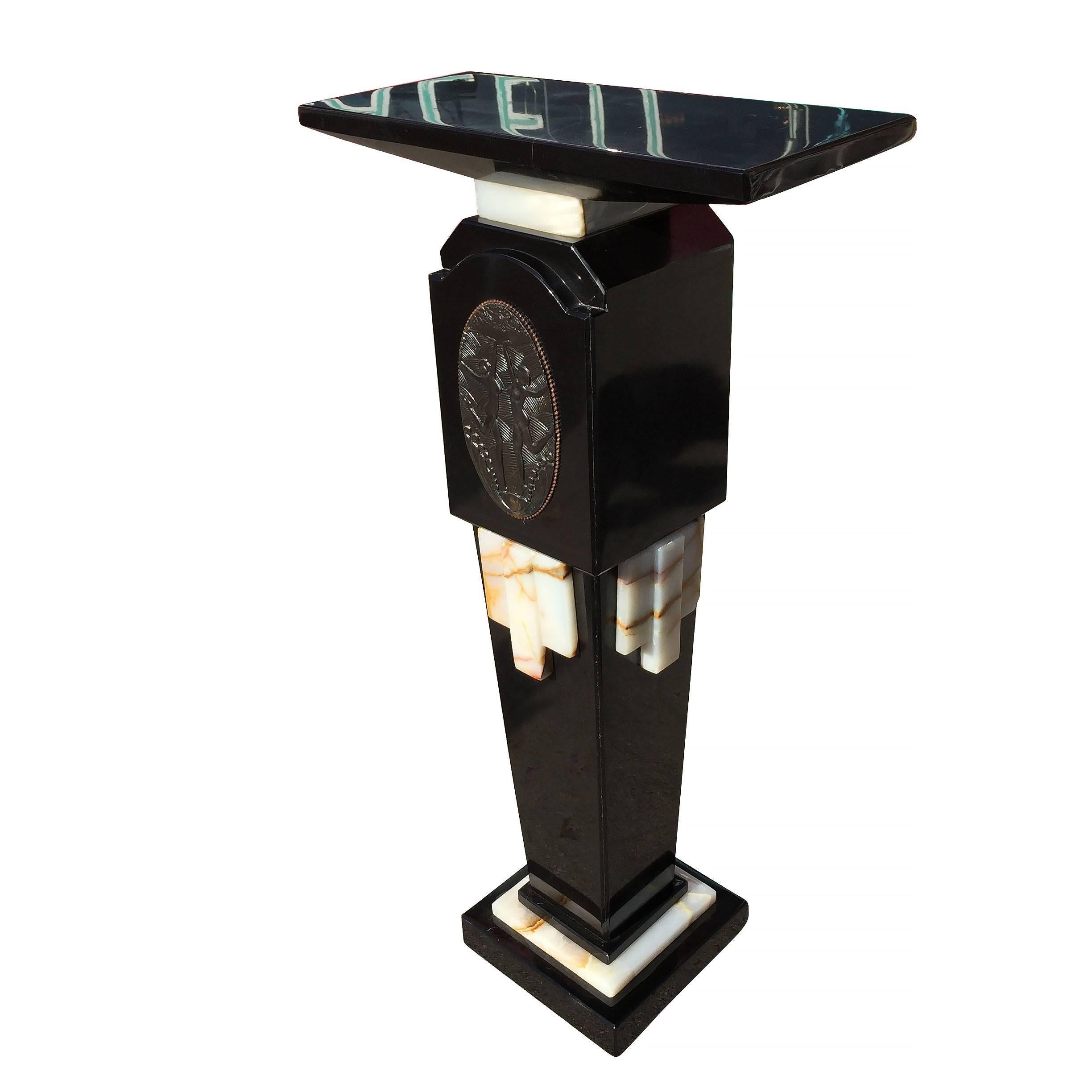Fine quality re-edition marble and bronze pedestal in the style of Chiparus featuring a mirror polished black marble pedestal with white onyx accents and stepped design. Front and center of the stand is a plaque applique made of bronze with two nude