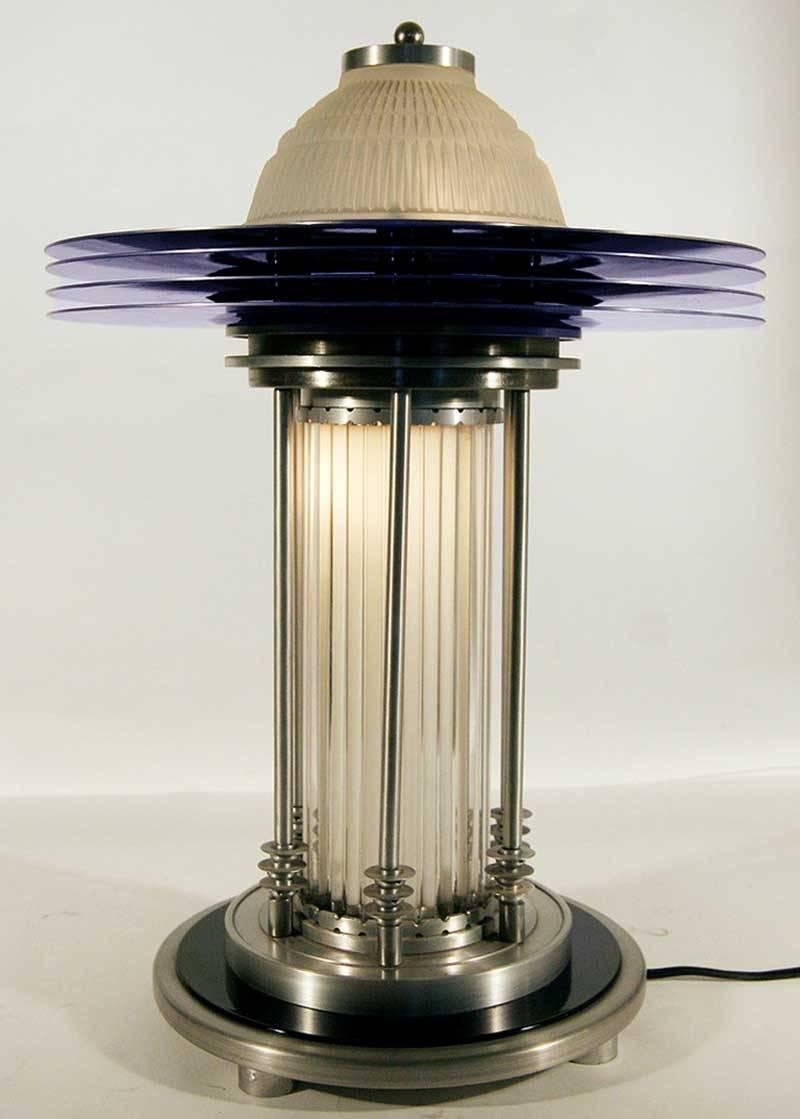 This stunning Art Deco style table lamp features a domed glass shade encircled by four anodized aluminum rings and held up by six aluminum poles.
