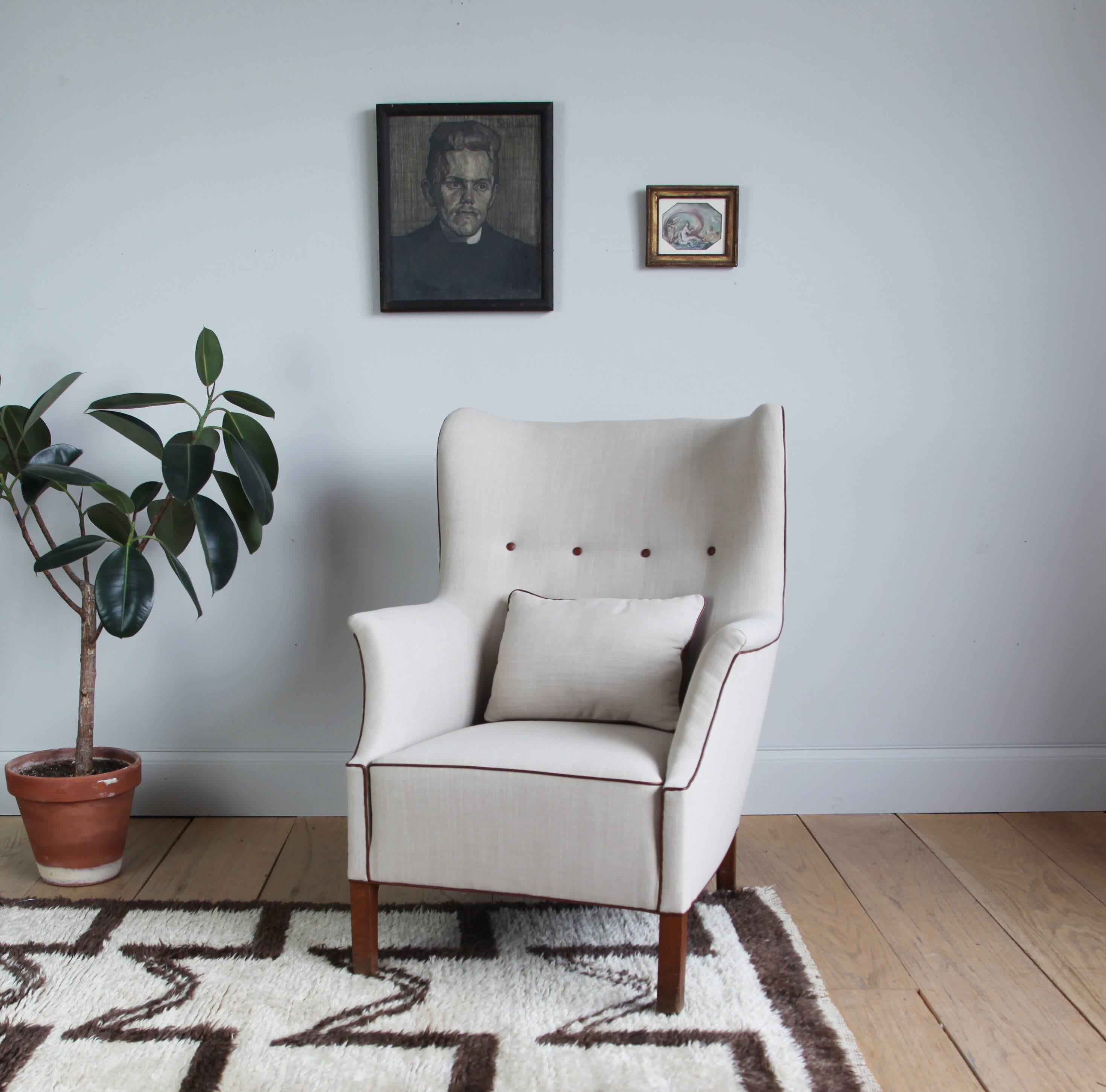 This capacious wingback chair was designed by Mogens Koch in 1936 for the City Hospital in Sønderborg, Denmark. It has been recently recovered in linen, with leather accents and a matching pillow.

In excellent vintage condition.