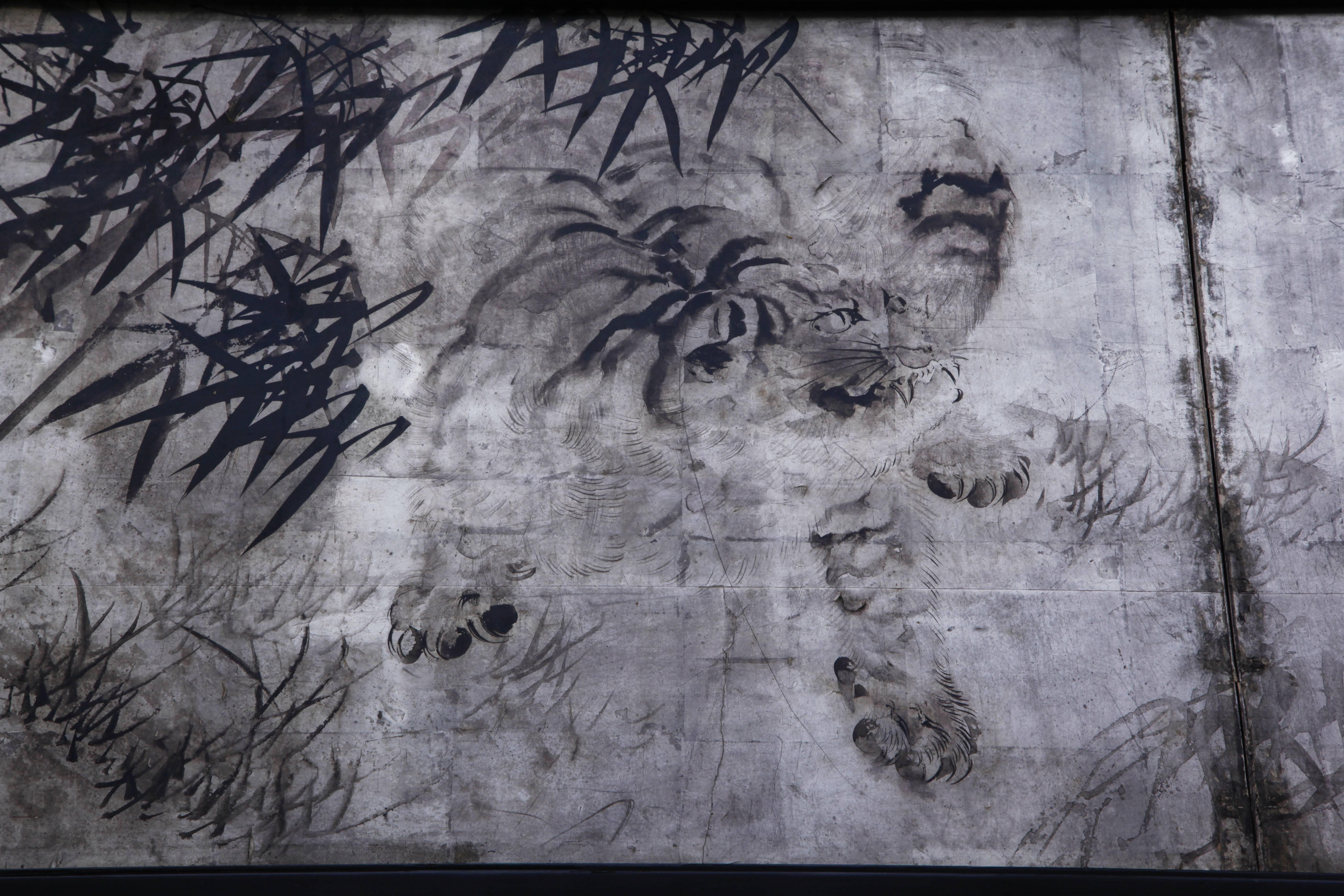A captivating two-fold paper screen, painted in black ink on silver ground, dated Spring 1912. The subject, a tiger crouching in bamboo, is portrayed with a spontaneous, natural energy; his mouth parted, tail switching, the bamboo leaves conveyed in