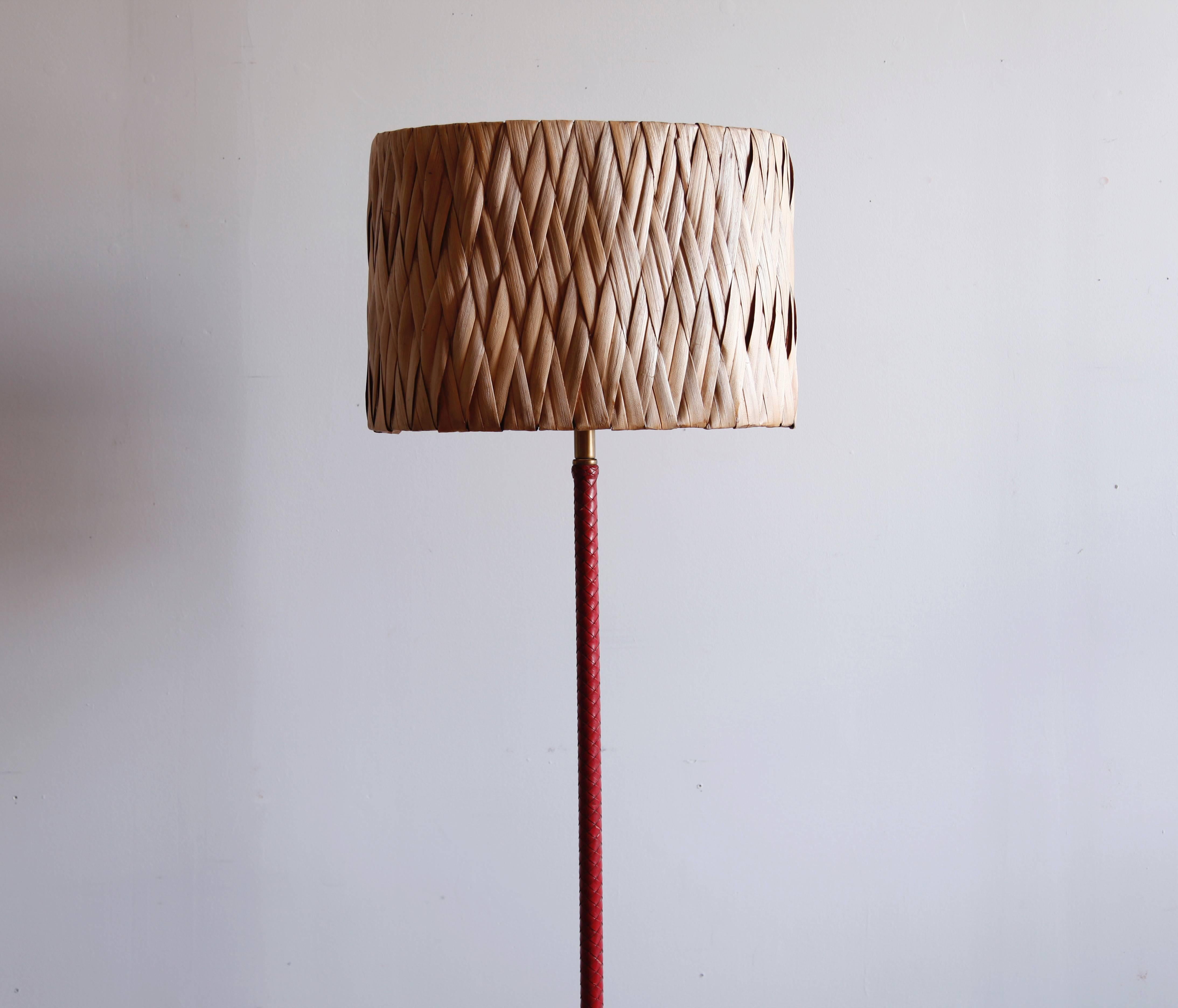 The leather braided over the brass stem of this lamp is an appealing oxblood color. Height is adjustable by a few inches. The vintage shade, braided palm leaf, is not sold with the lamp but pairs beautifully with it.