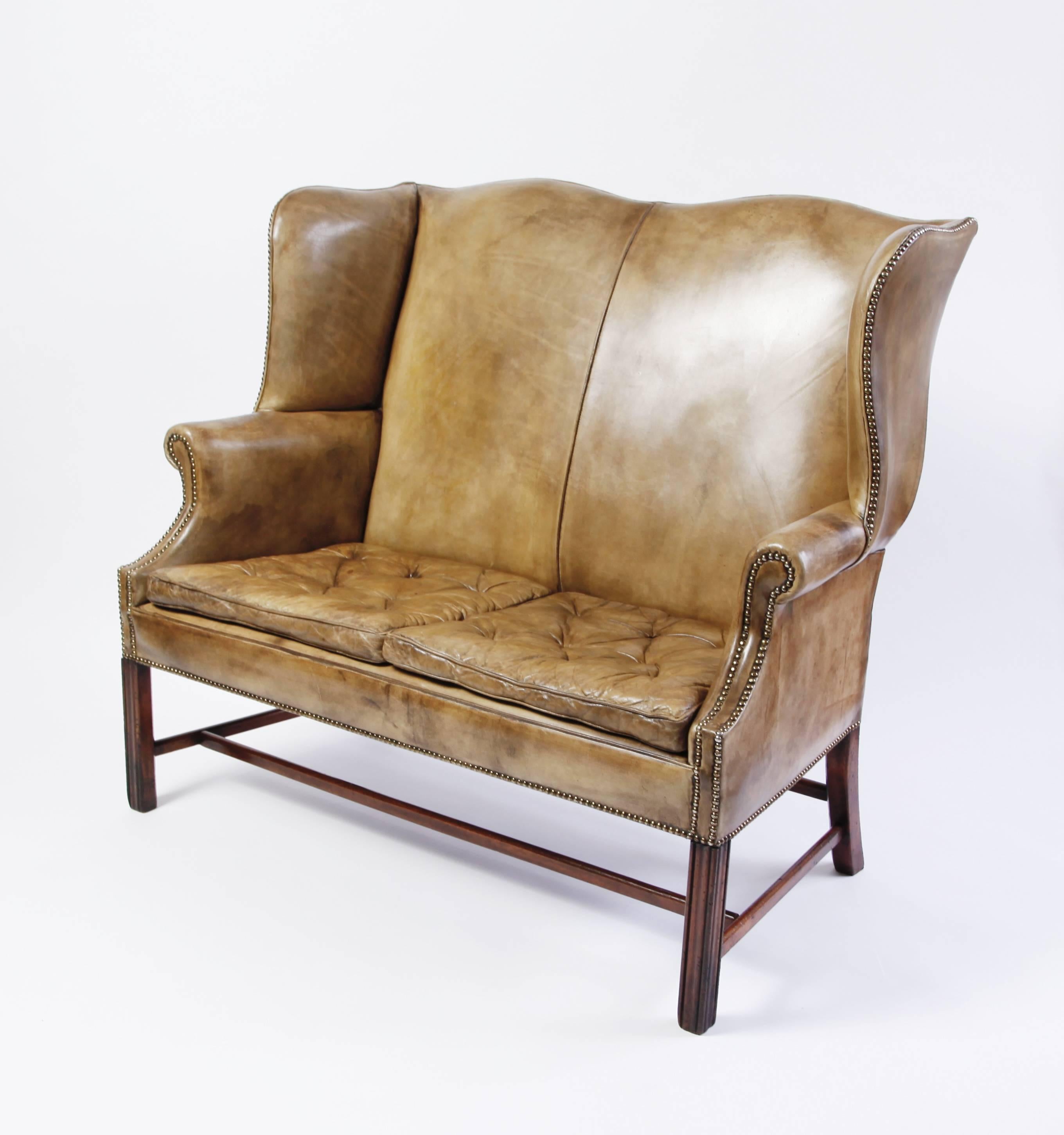 A curvaceous George III-style settee from the late 19th - early 20th century. Mahogany legs, wonderfully patinated original leather. 