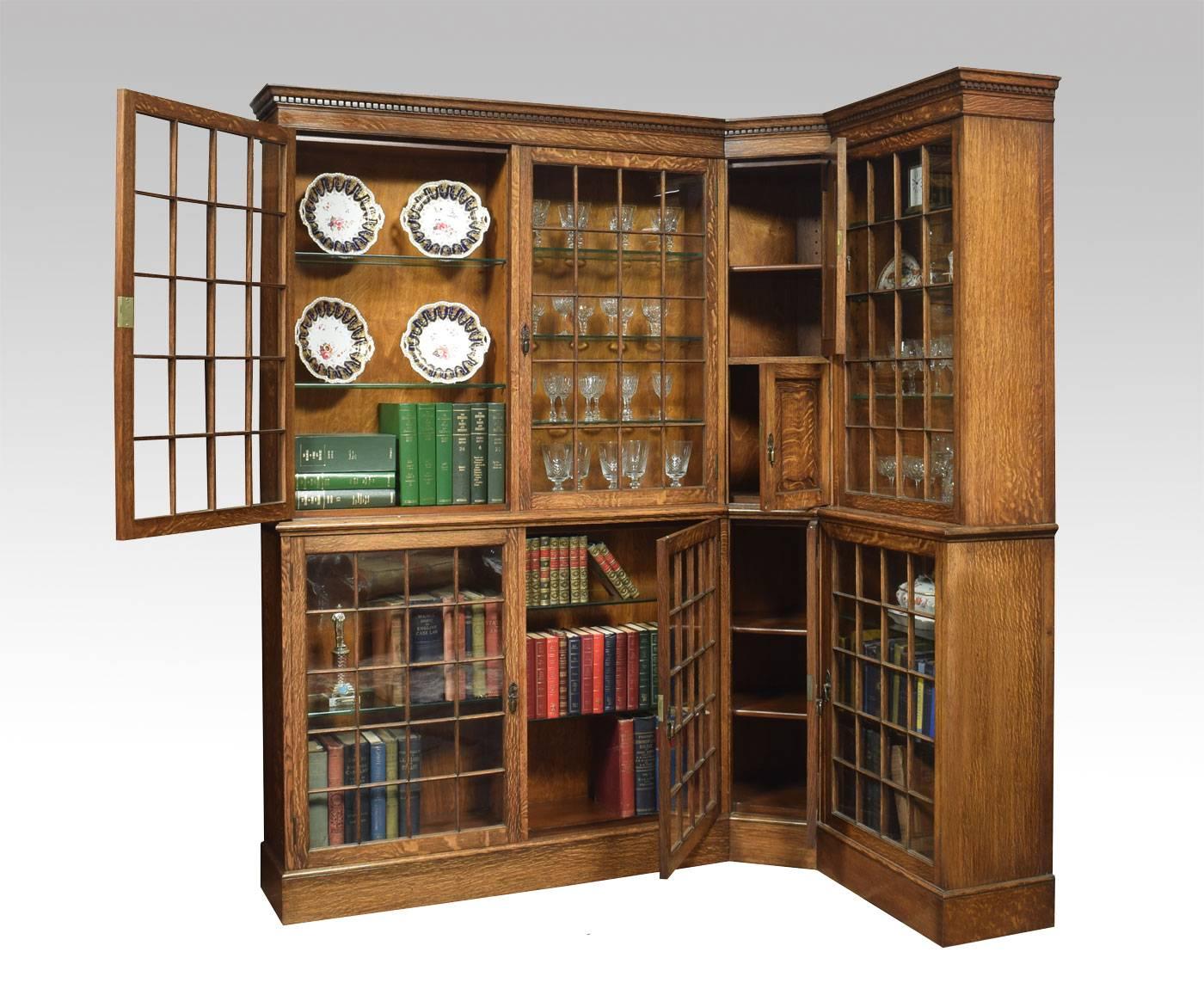 
Oak corner bookcase having flared dentil cornice, above glazed panel doors enclosing adjustable glazed shelves with central fielded paneled oak doors enclosing adjustable shelves. The base section with similar glazed and paneled doors. All raised