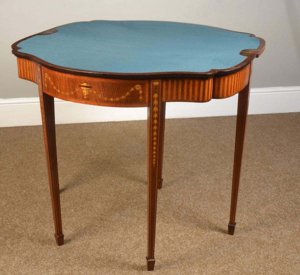 

Mahogany and marquetry serpentine card table in the Sheraton manner the satinwood-banded top inlaid with a fan medallion and radiating husk chains, the frieze with simulated fluting on urn and husk chains and on tapering square legs with spade
