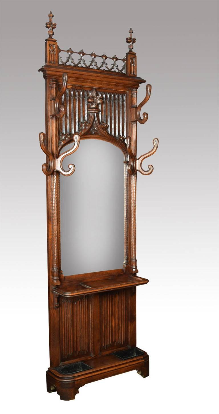 Victorian Gothic oak hall stand, having the poppy finials and pierced top with tracery arches to the back having large original mirror plate surrounded with unusual S-shaped hooks on carved columns above an umbrella Stand with original drip