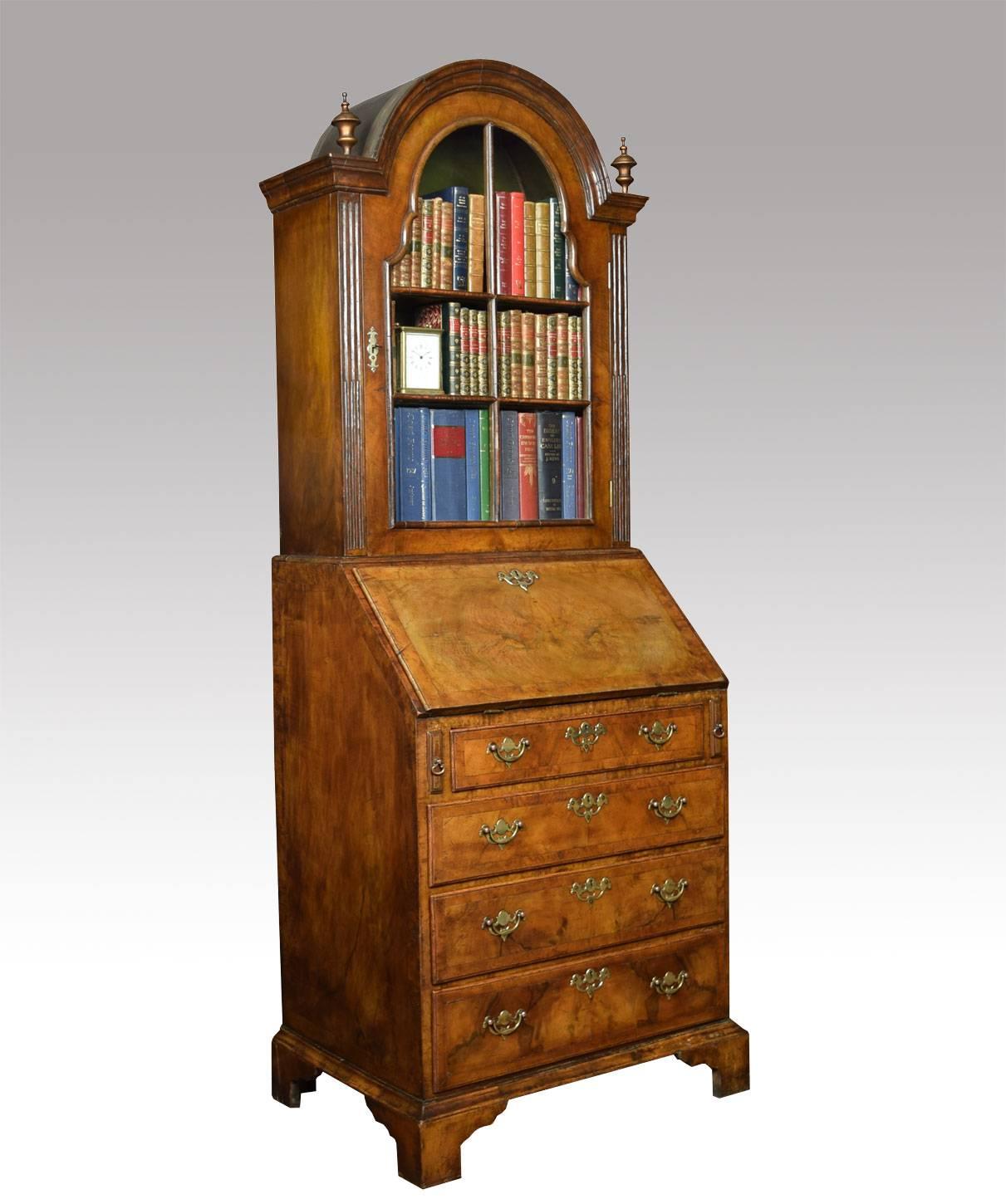 

Queen Ann style walnut bureau bookcase of small proportions, the arched and moulded pediment flanked by urn finials above single glazed door opening to reveal shelved interior. The base fitted with a fall flap enclosing a fitted interior of