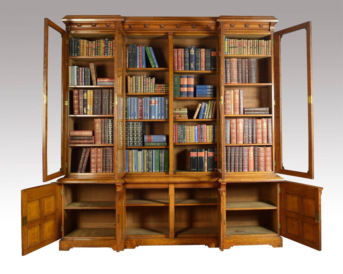 Large oak bookcase the carved molded cornice above four large glazed doors each section fitted with four adjustable shelves. The base section fitted four paneled doors opening to reveal single adjustable shelf to each section all raised up on plinth