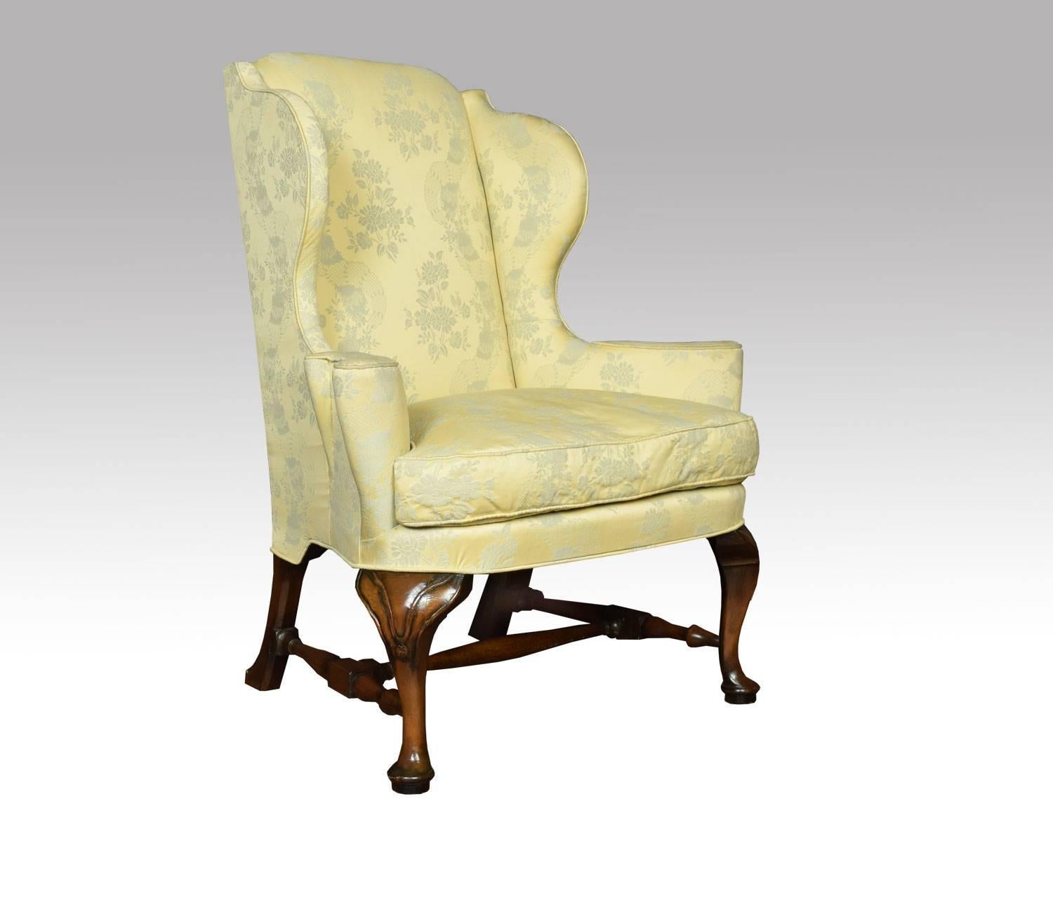 Early 20th century Queen Anne style wing armchair having walnut front carved cabriole legs, with swept legs to the rear united by stretcher. The wing armchair upholstered in damask upholstery having removable cushion.

Dimensions:

Height 44