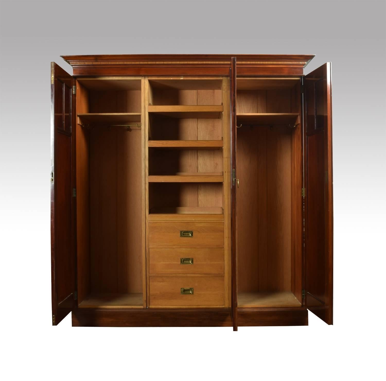 Maple & Co Edwardian mahogany three-door wardrobe the projecting cornice above center mirrored door enclosing linen trays and drawers flanked by a pair of floral marquetry inlaid doors enclosing hanging space. All raised up on plinth