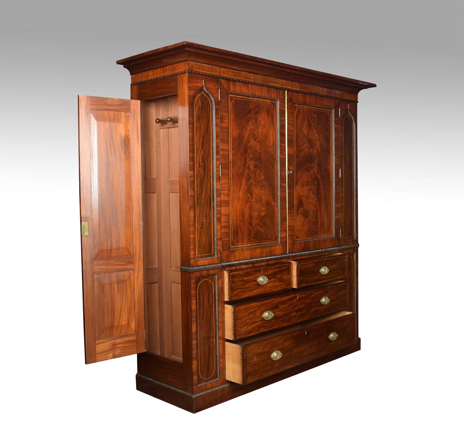 William IV string inlaid wardrobe. The moulded cornice above two mahogany panelled doors opening to reveal five sliding trays. The base section fitted with two short and two long graduated draws all with lion mask handles. The sides are fitted with