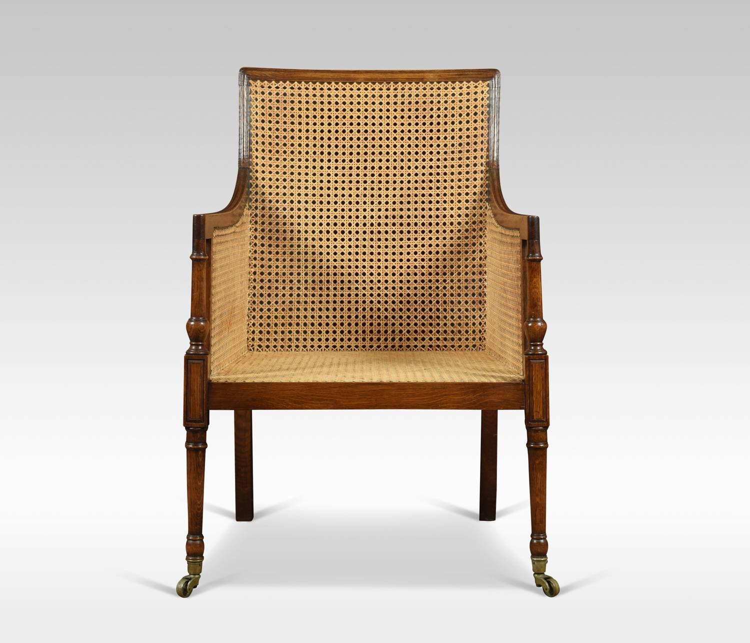 Bergère armchair, the solid oak frame and inset bergère back and seat with removable black leather cushion. Raised up on turned tapering legs. Terminating in brass caps and castors.

Dimensions
Height 36 inches, height to seat 17 inches
Width 23