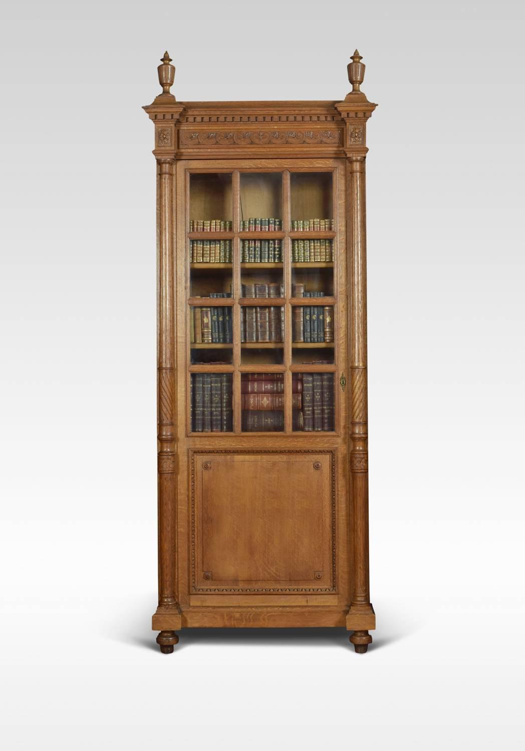 Pair of tall alcove oak bookcases, having large urn finials above carved dental moulded freeze. To the large rectangular doors with glazed top section and oak panel below. Opening to reveal adjustable shelved interior, (each bookcase having five