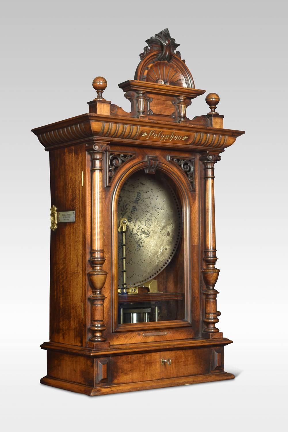 An upright walnut polyphon playing 20 inch interchangeable metal discs, with a crank wound movement and coin slots either side with signs stamped ‘Drop a Penny in the Slot’, the walnut case having a decorative pediment to the top with shell