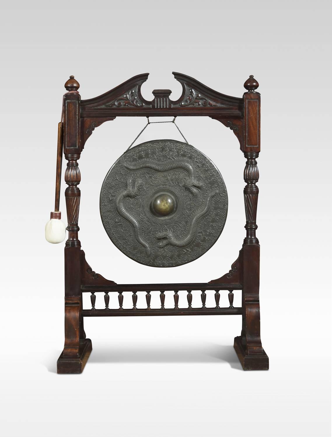 Walnut framed floor standing diner gong and beater, the broken arch crest, flanked by turned finials raised on reeded carved pillars and a bobbin turned gallery below, raised on splayed legs and platform feet. The 18 Inch bronze plate cast in