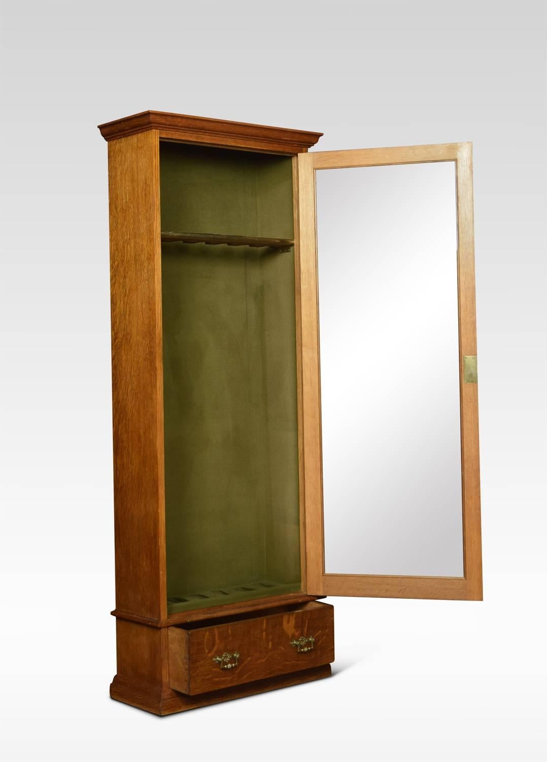Late Victorian oak floor standing gun display cabinet, the large single glazed door opening to reveal gun rests, over a short drawer to the base. Fitted with brass handles and opening to reveal an ivorine label for Army and Navy