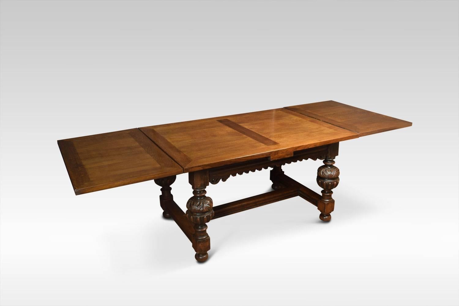 An Impressive Elizabethan style oak draw-leaf table of generous proportions. The thick plank top having pull-out leaves to each end above strap-work frieze with scrolling foliated carving raised on bulbous cup and cover legs leading down to block