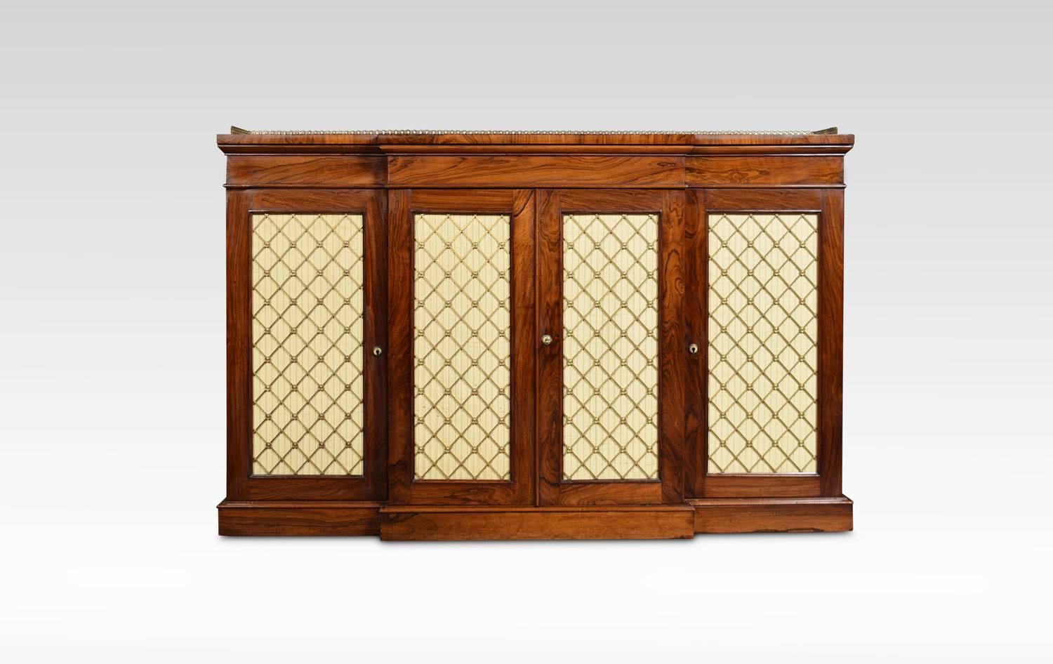 Impressive George IV side cabinet, the large breakfront rosewood top having raised three quarter pierced brass gallery, over four cupboard doors with original brass lattice grills and silk backing. Opening to reveal adjustable shelved interior. All