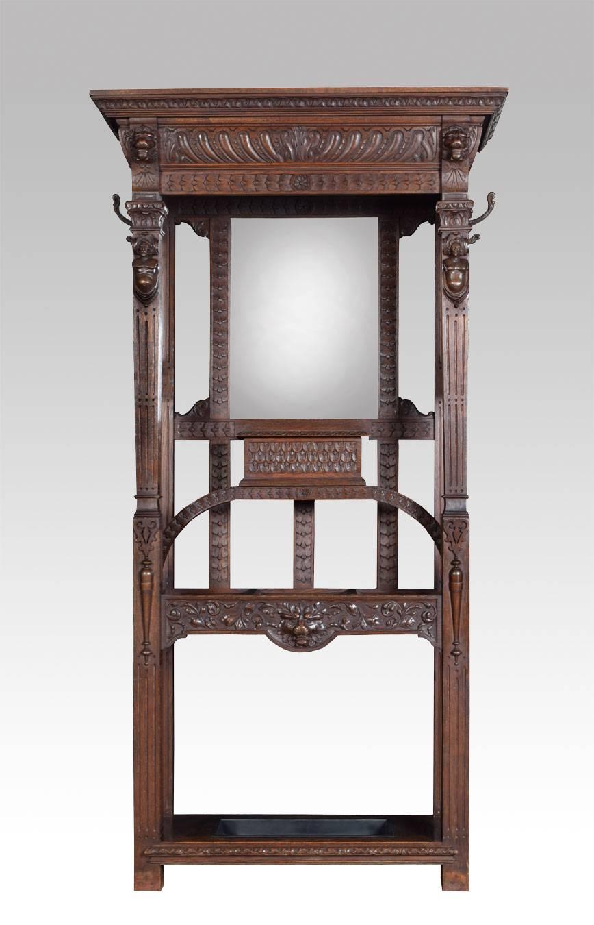 Gothic carved oak hall stand, the protecting cornice above mirrored back flanked by profusely carved pillars with busts and lion masks, the base section fitted with lidded glove compartment above stick stand having drip tray