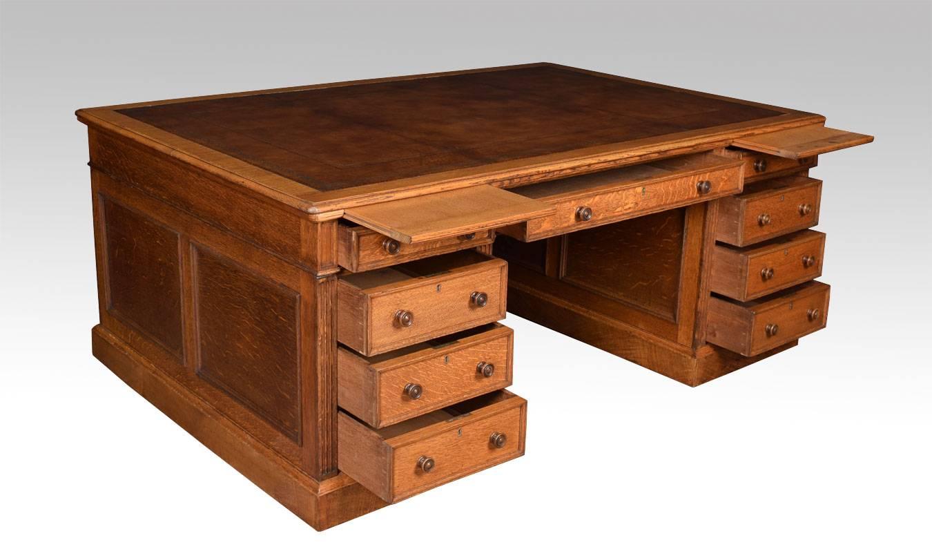 Very large oak partners/library desk By Maple & Co the rectangular brown hide top with a gilt-tooled border enclosed by a moulded edge over an arrangement of three freeze drawers above two large pedestals having brush in slides and three draws to