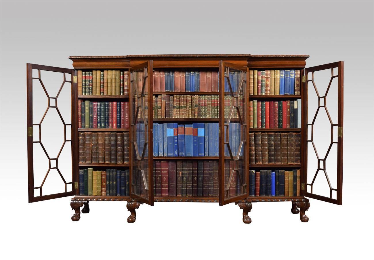 

mahogany breakfront glazed bookcase, the large rectangular top having carved moulded edge to two glazed beaded doors flanked by two further glazed doors all sections fitted with three adjustable shelves. All raised up on six ornately carved